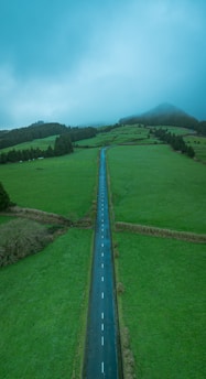 Road stretches through green fields on a cloudy day.