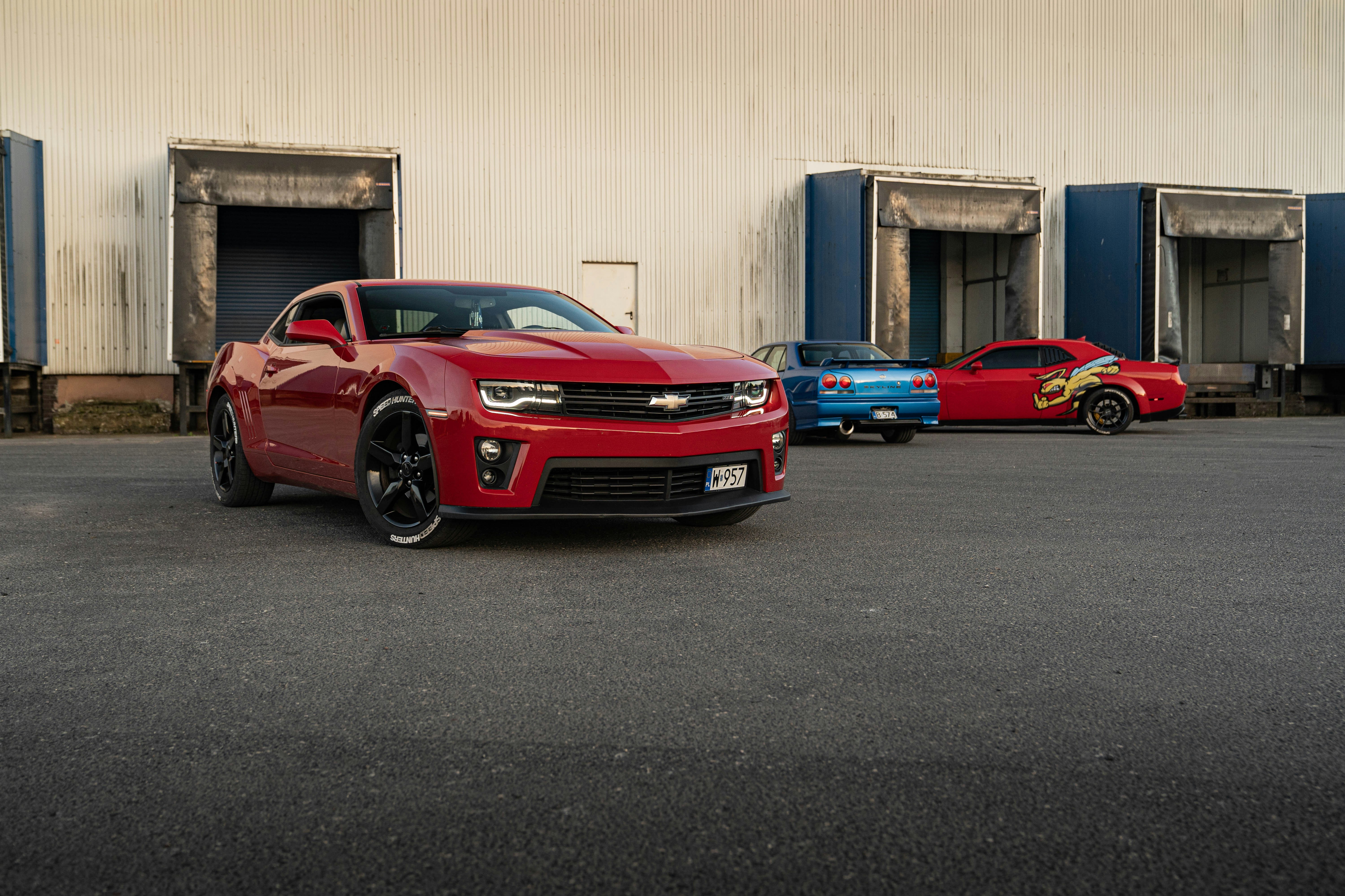 A red camaro is parked with two others.
