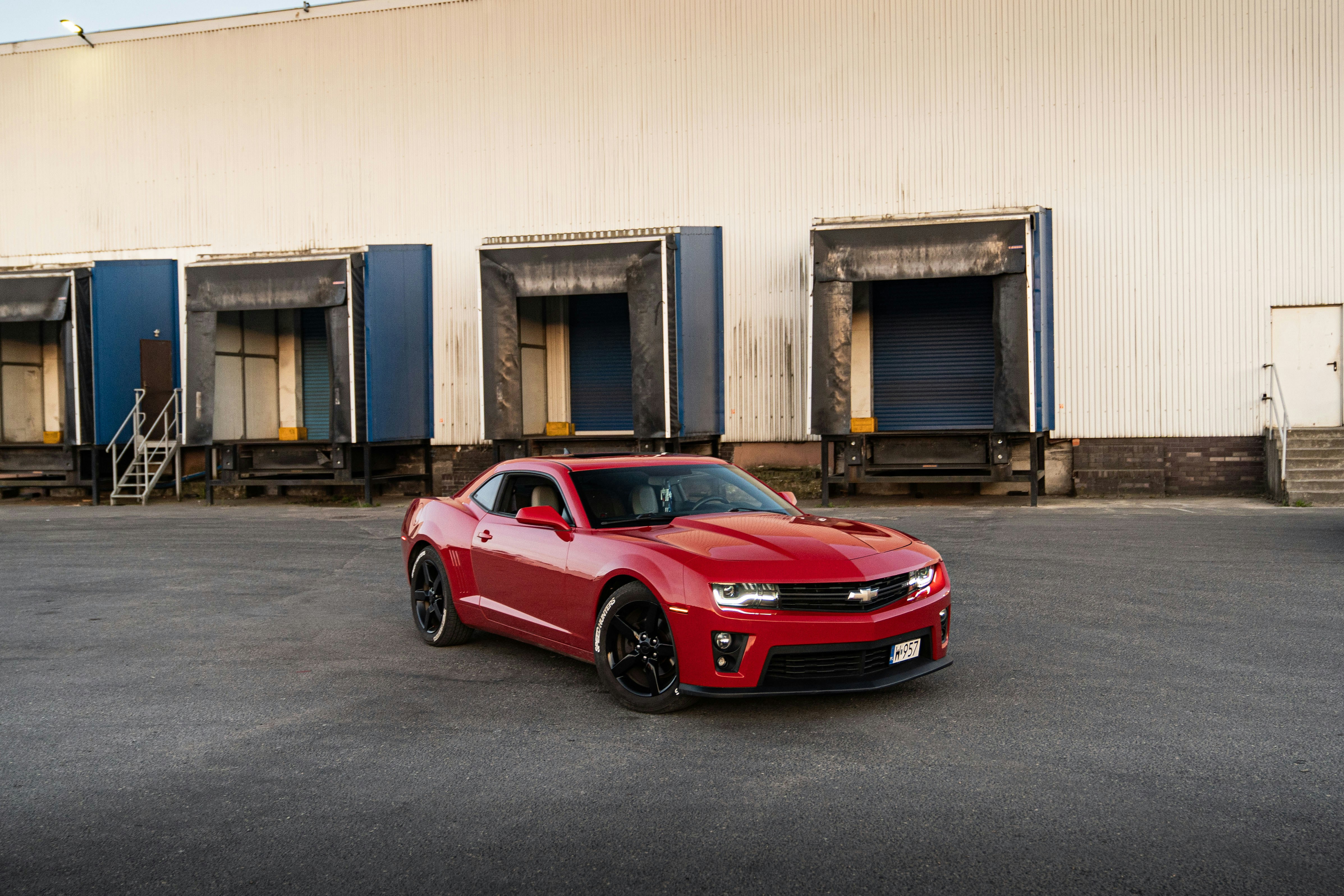 A red chevrolet camaro parked in front of a warehouse.