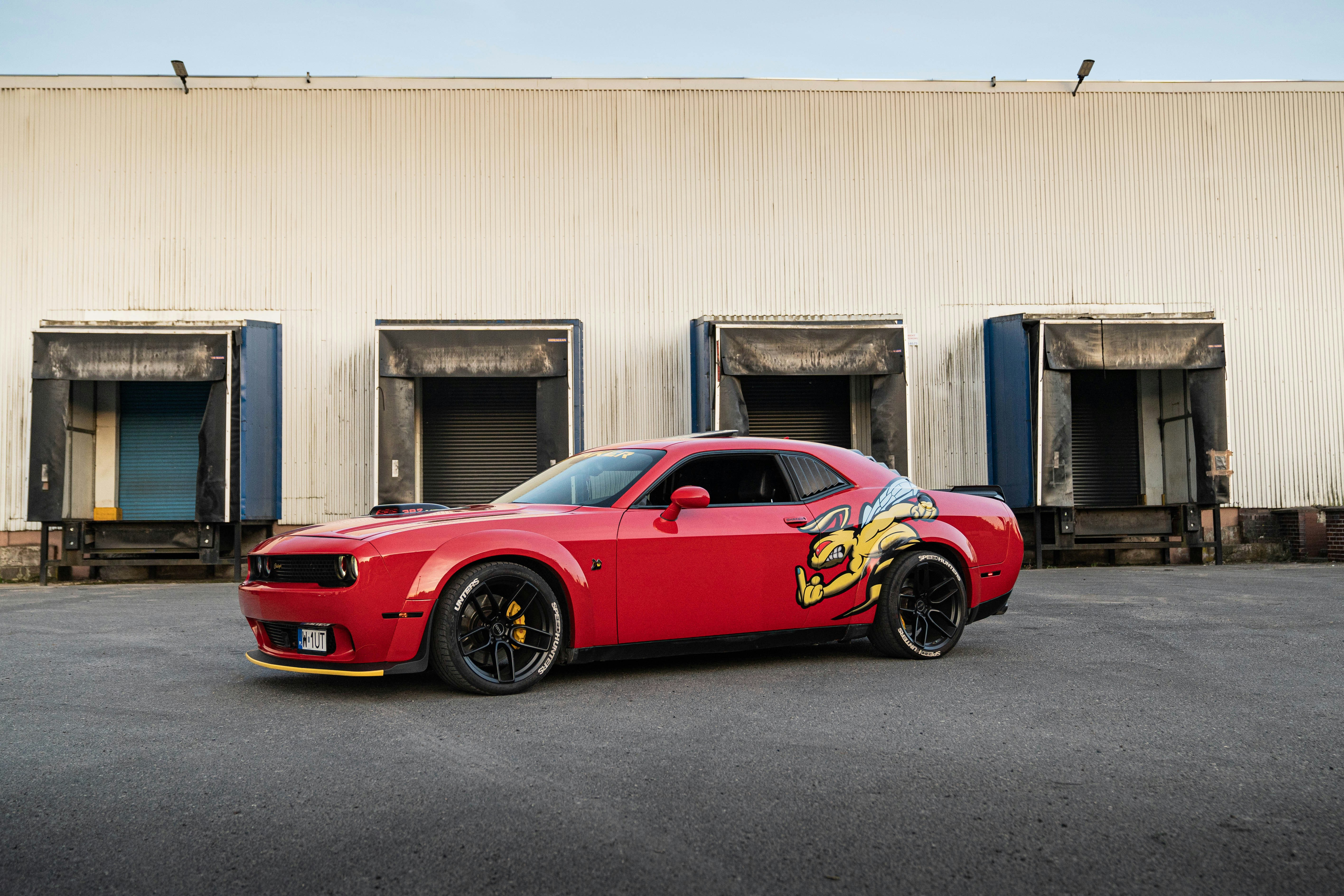 A red dodge challenger is parked by loading docks.