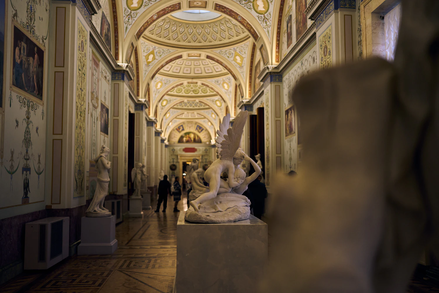 A vaulted gallery with gilded ceiling decoration and a sculpture in the foreground