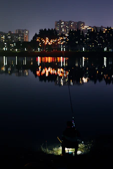Carp angler fishing by the lake at night, bite alarms on bank sticks