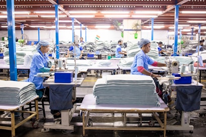 Workers sew textiles in a large factory setting.