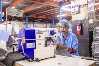 A woman sews with a button attaching sewing machine in a garment factory.