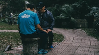 Two men sit on a stone bench outside.