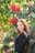 Woman smiles next to beautiful red flowers.