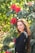 Woman smiles next to beautiful red flowers.