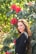 Woman smiles next to beautiful red flowers.