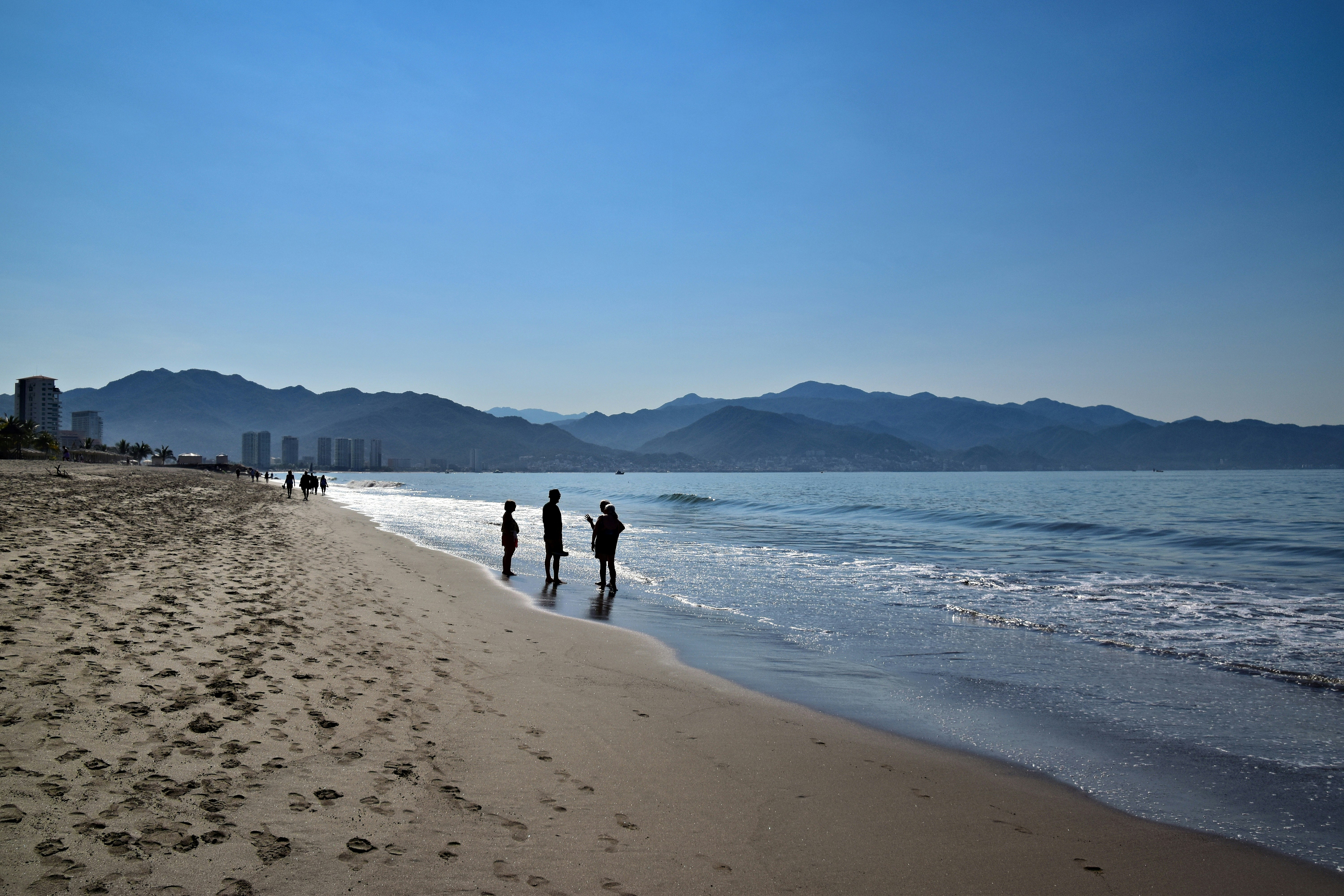 People walk along a beach with mountains in the background
