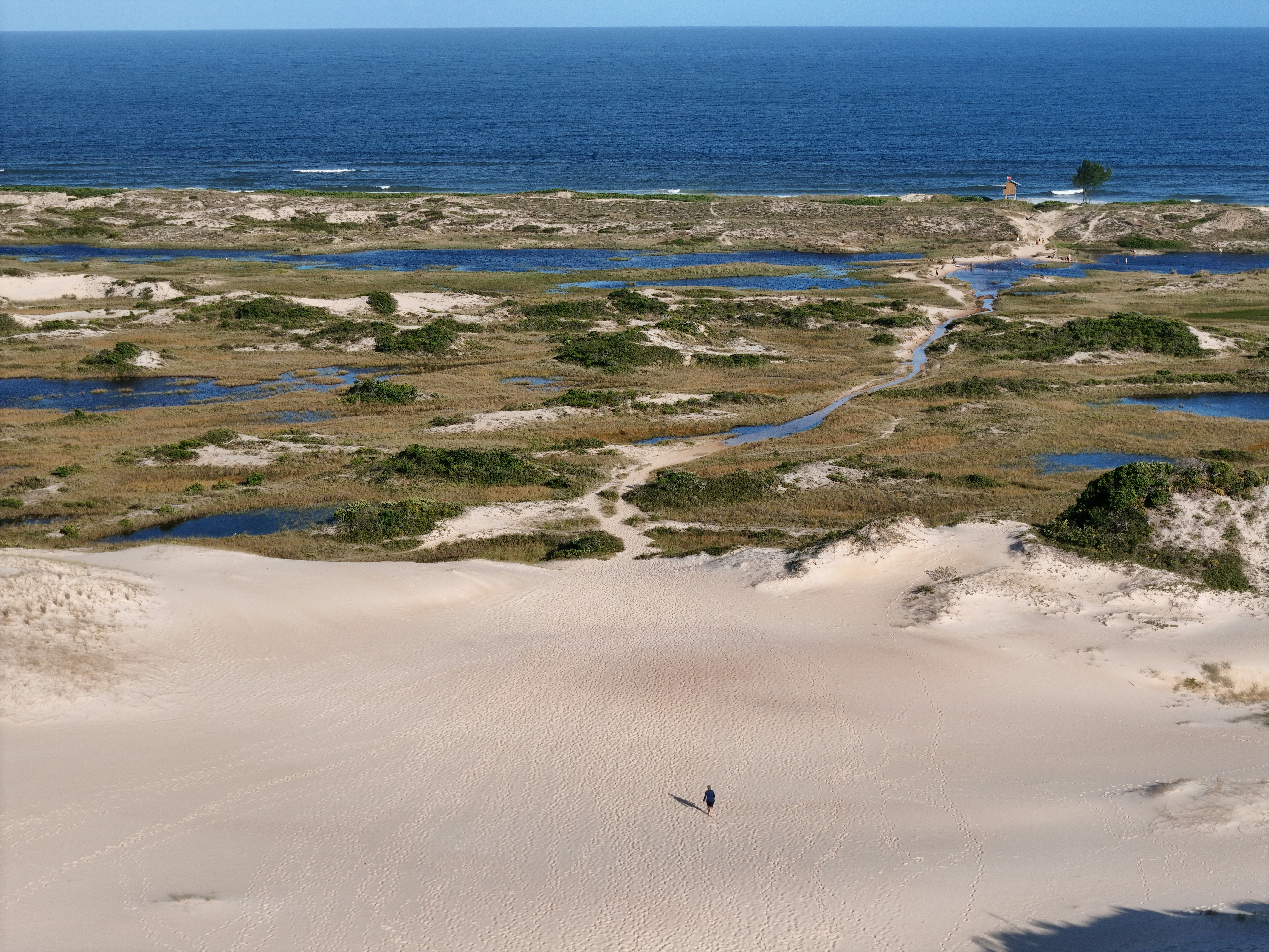 Sandy dunes and water meet the vast blue ocean.
