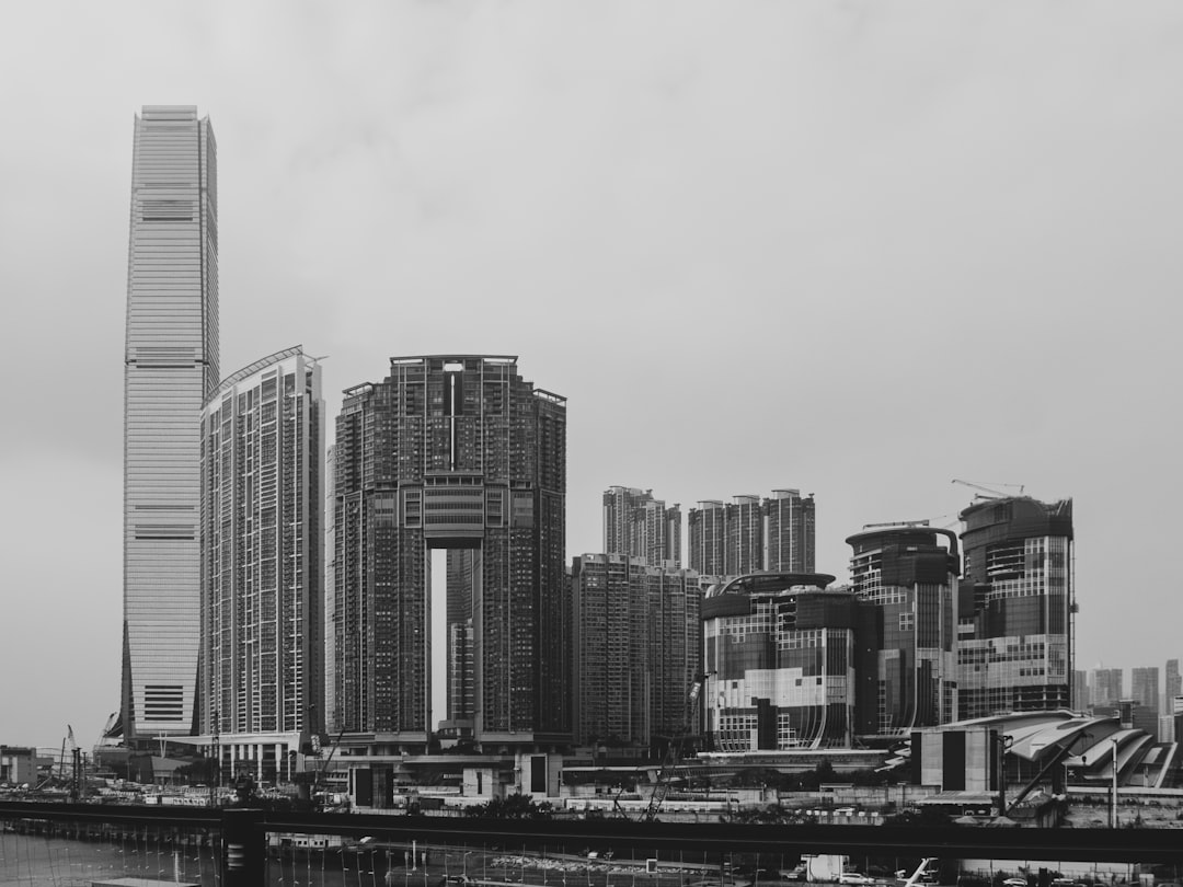 A black and white cityscape of modern buildings., The skyline above Kowloon Station and Union Square features prominent skyscrapers, including the International Commerce Centre—the tallest building in Hong Kong—as well as the luxury residential towers, the Arch and the Harbourside, on the left side of the photo. As new constructions emerge in this concrete jungle, they evoke a sense of both relentless development and a feeling of overwhelmingness.