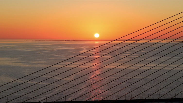 Sunset over the water with a bridge's cables.