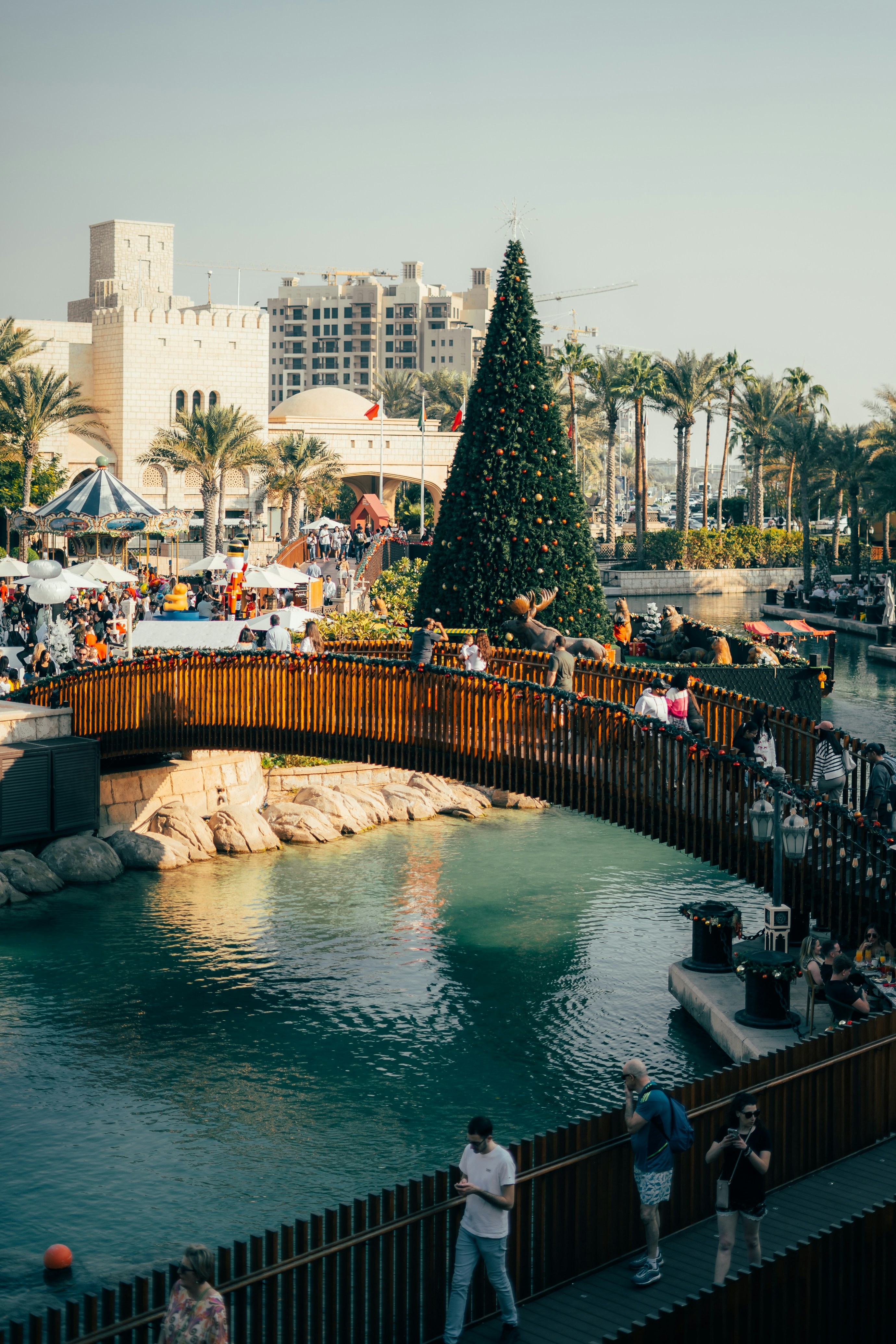 A christmas tree stands on a bridge over water.