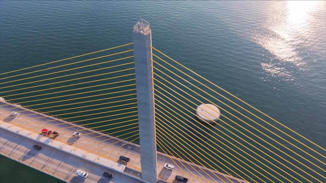 A suspension bridge and highway above water., A dramatic aerial close-up of the Sunshine Skyway Bridge, showcasing its towering central pylon and golden cables against the shimmering waters of Tampa Bay.
