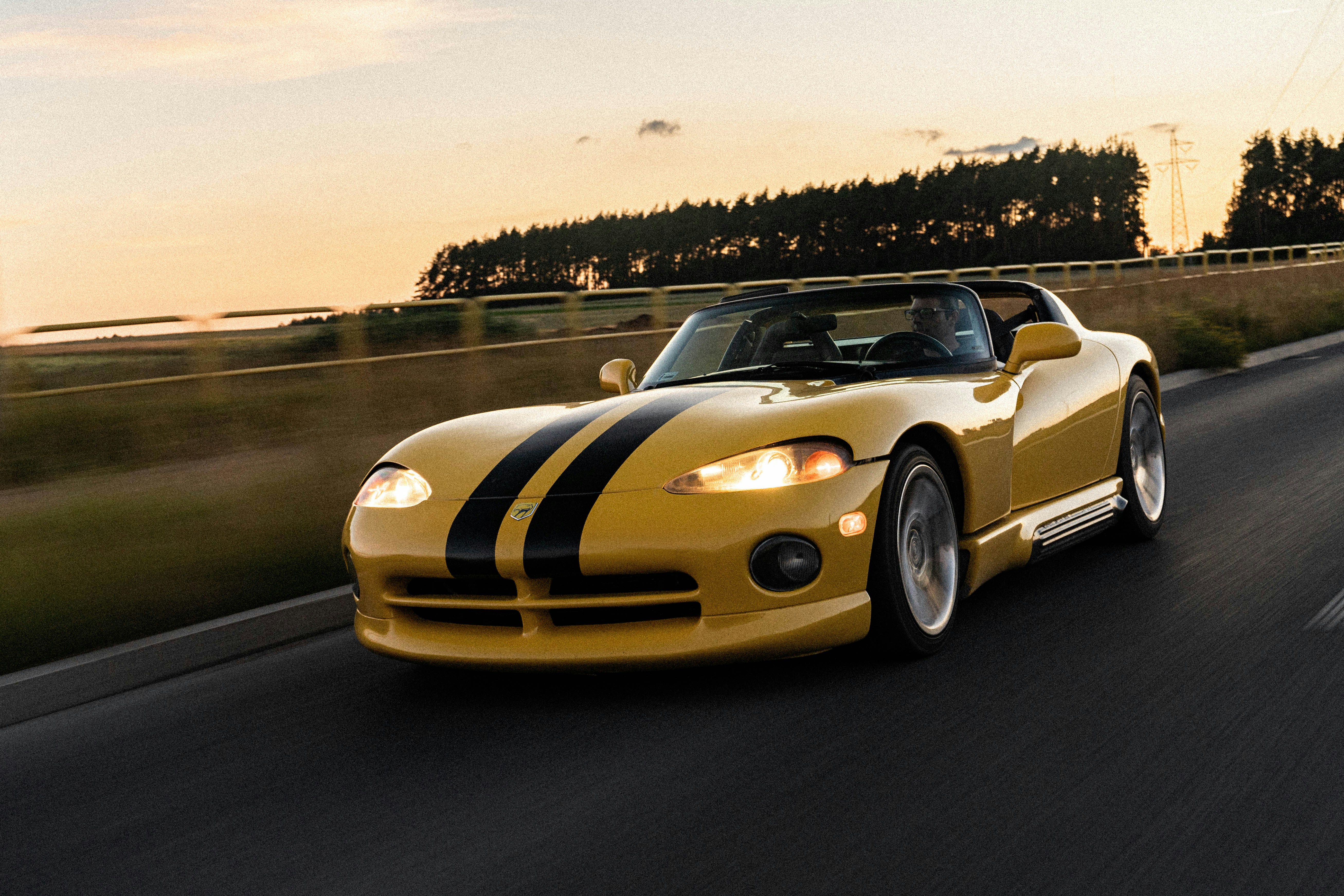 Yellow dodge viper with black racing stripes on the road.