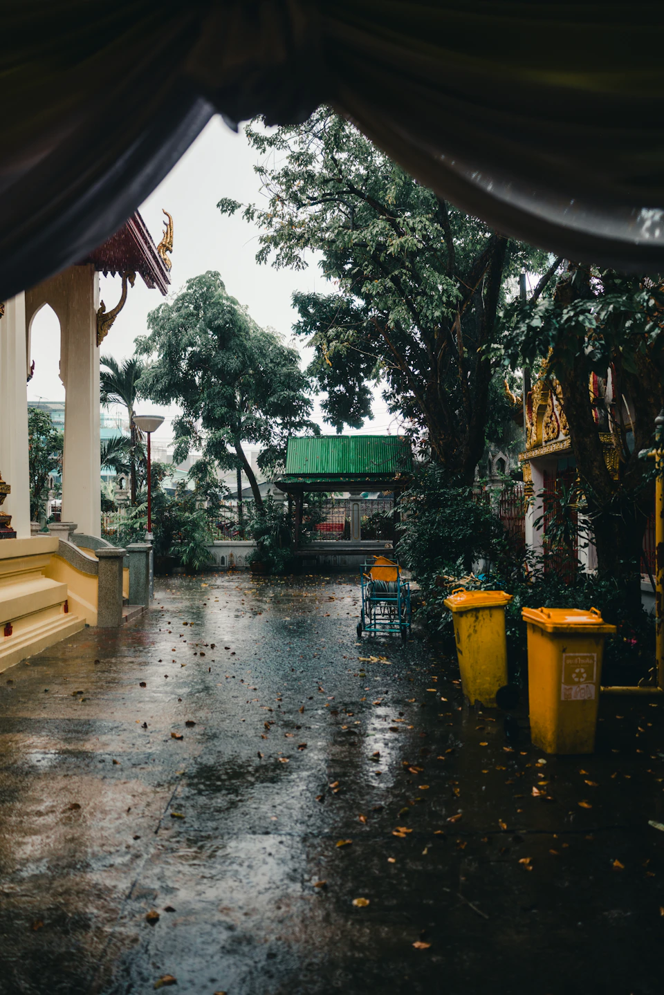 A Bangkok temple courtyard with ornate spires reflected in pooled water after a monsoon rain shower