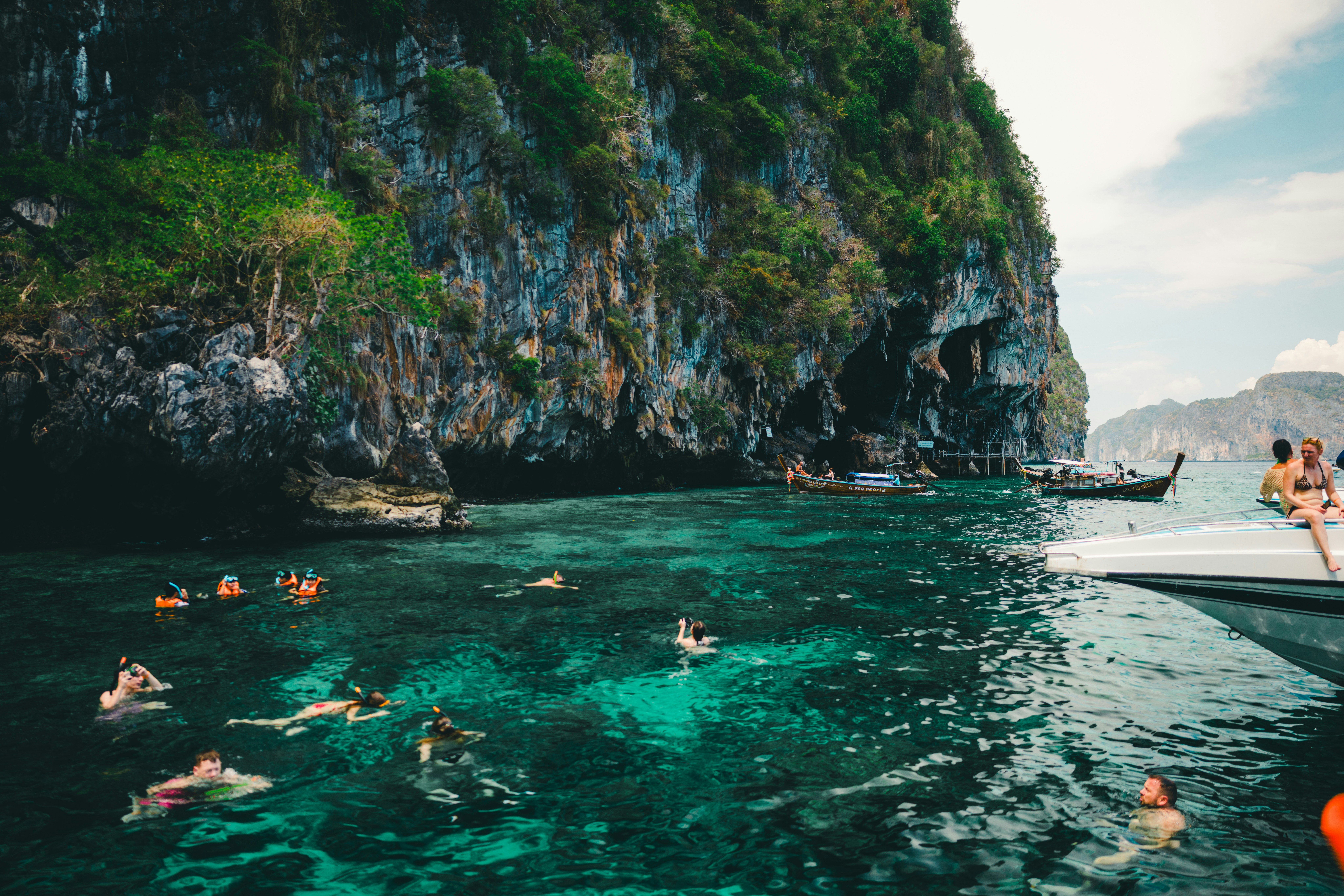 People snorkel in the turquoise water near a cliff.