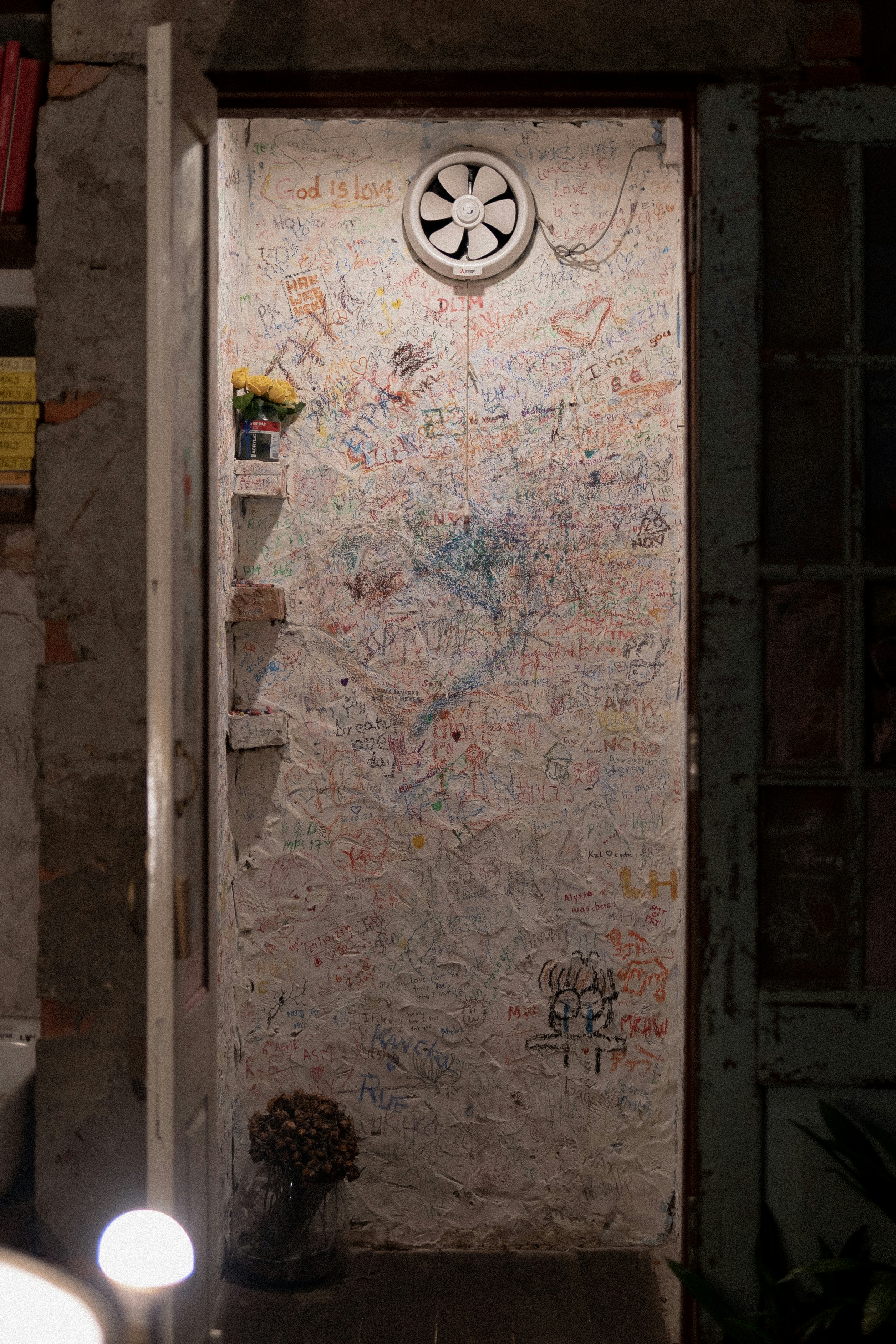 A doorway is covered in graffiti, with a fan.