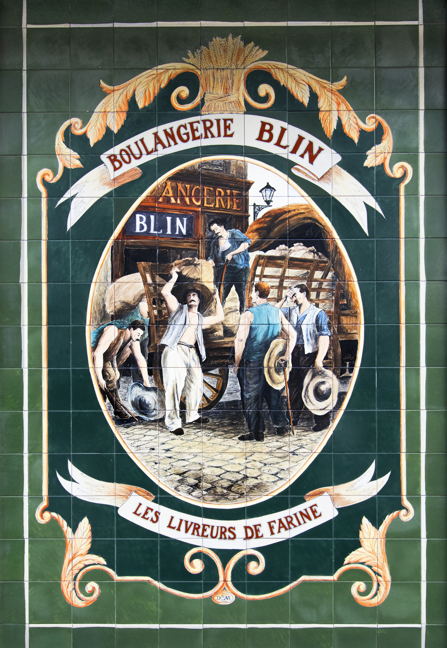 A painted green tile mural advertising a boulangerie, with a street scene in an oval frame and a French caption on a ribbon