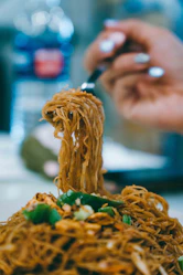 Noodles are lifted from the plate with a fork.