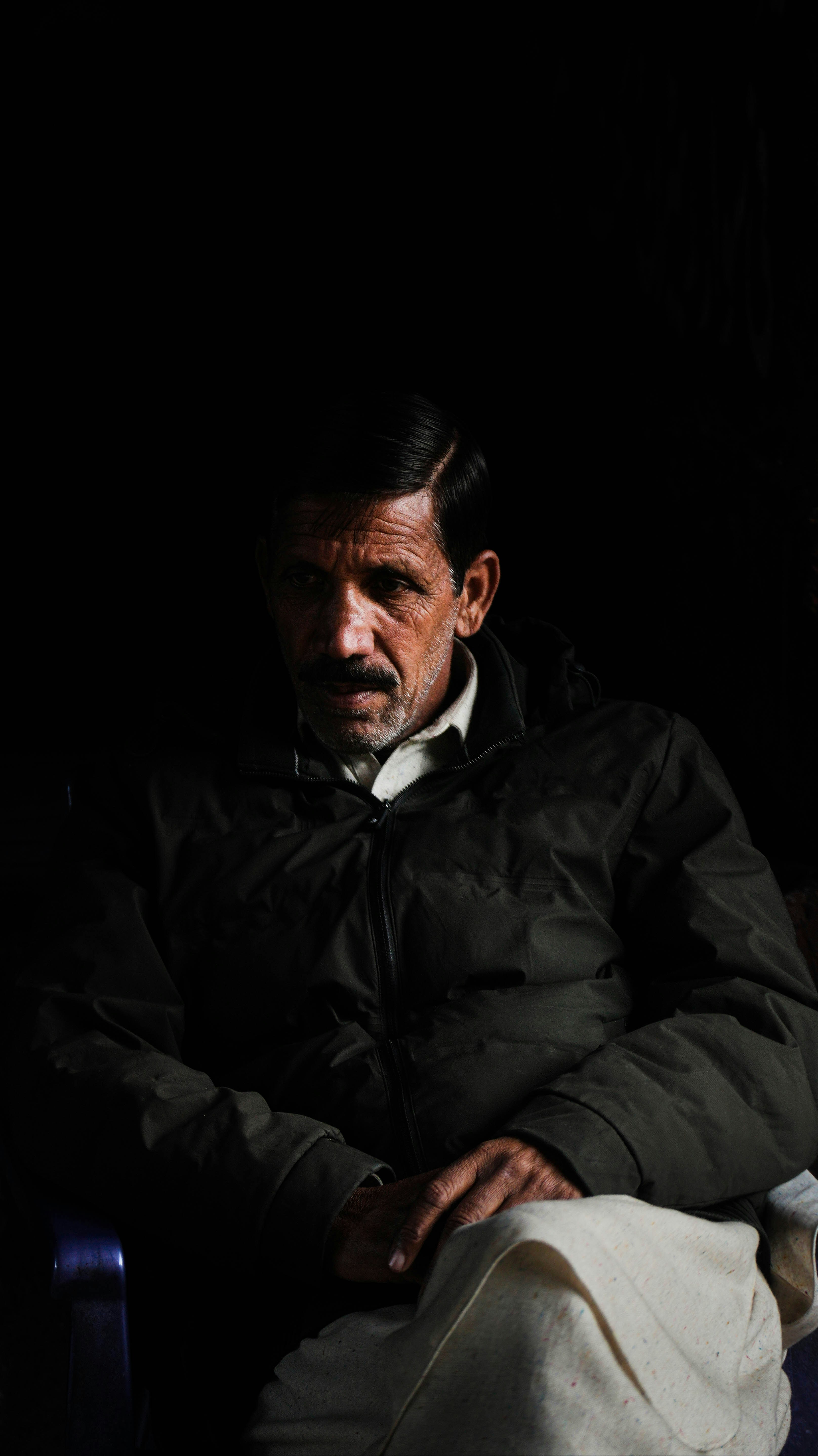 A man sits, lit against the dark background.