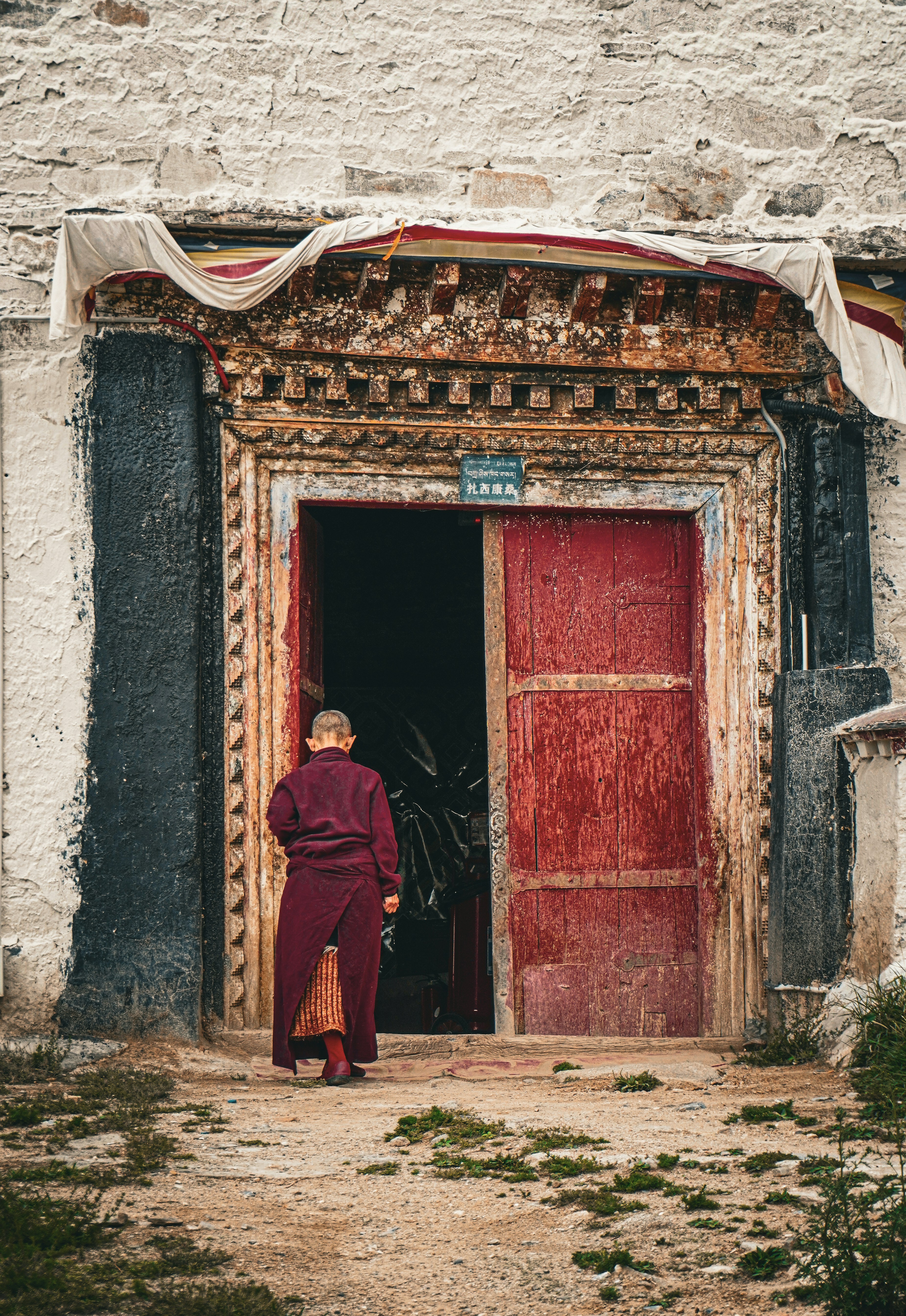 Monk enters a building through a red, ornately decorated doorway.