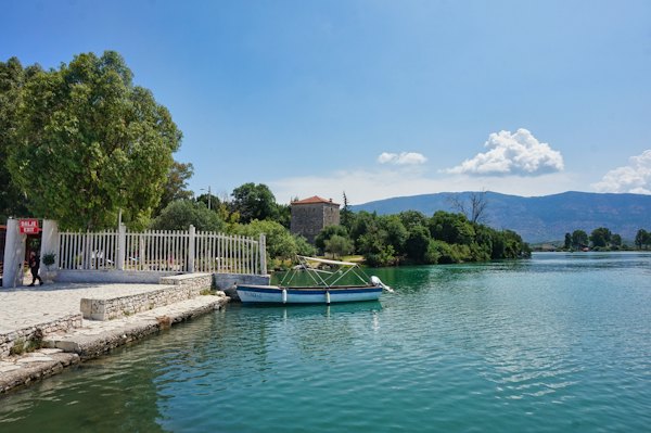 A peaceful lake scene with mountains and a boat — Sarandë, Albania