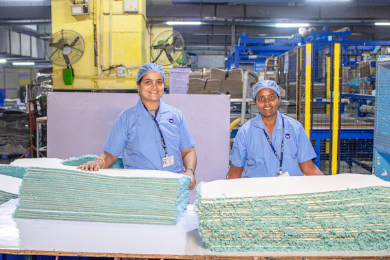Two workers stand in a factory, smiling.