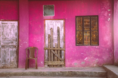 A pink wall has doors, windows, and a chair.