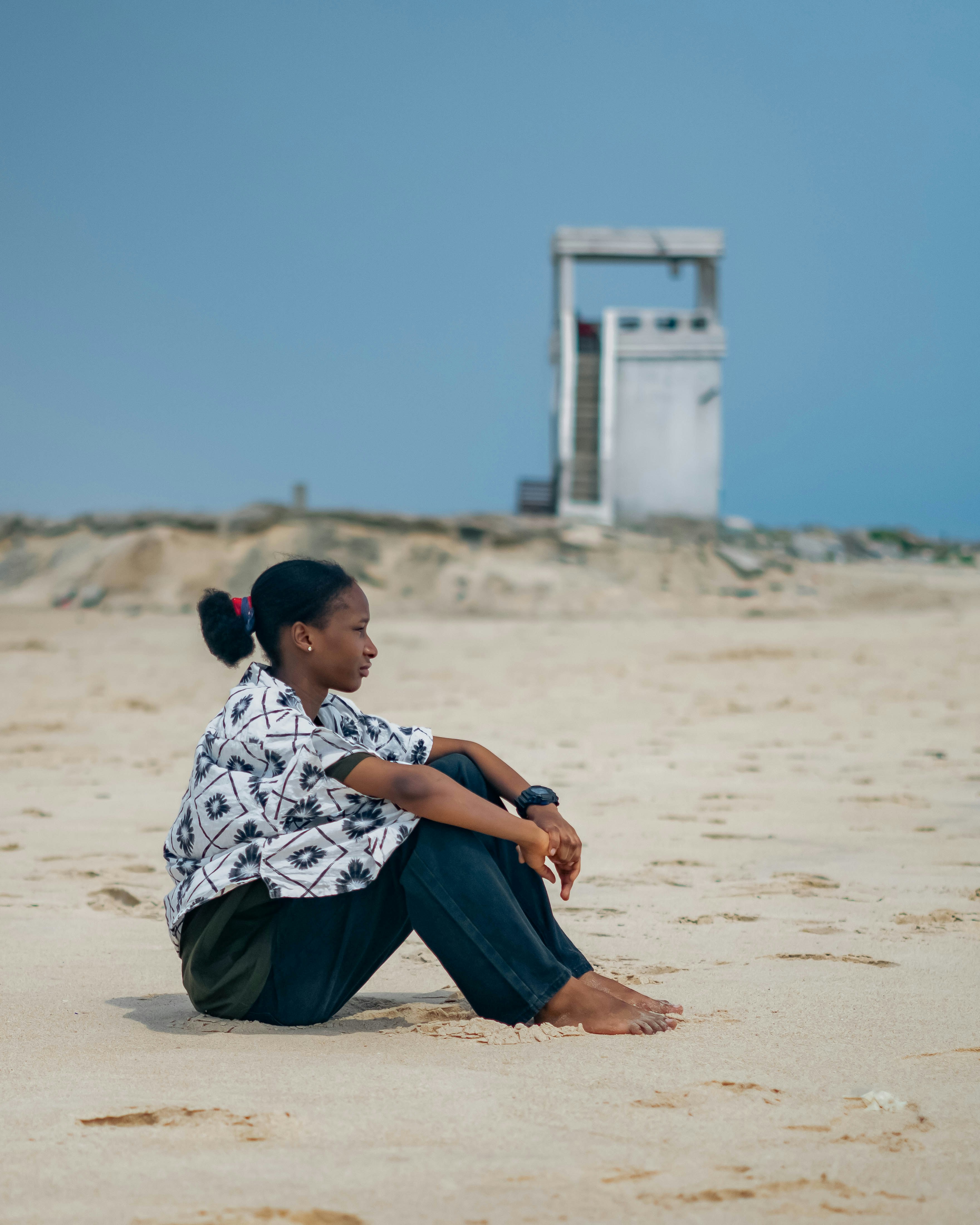 Woman sits on the beach, lost in thought.