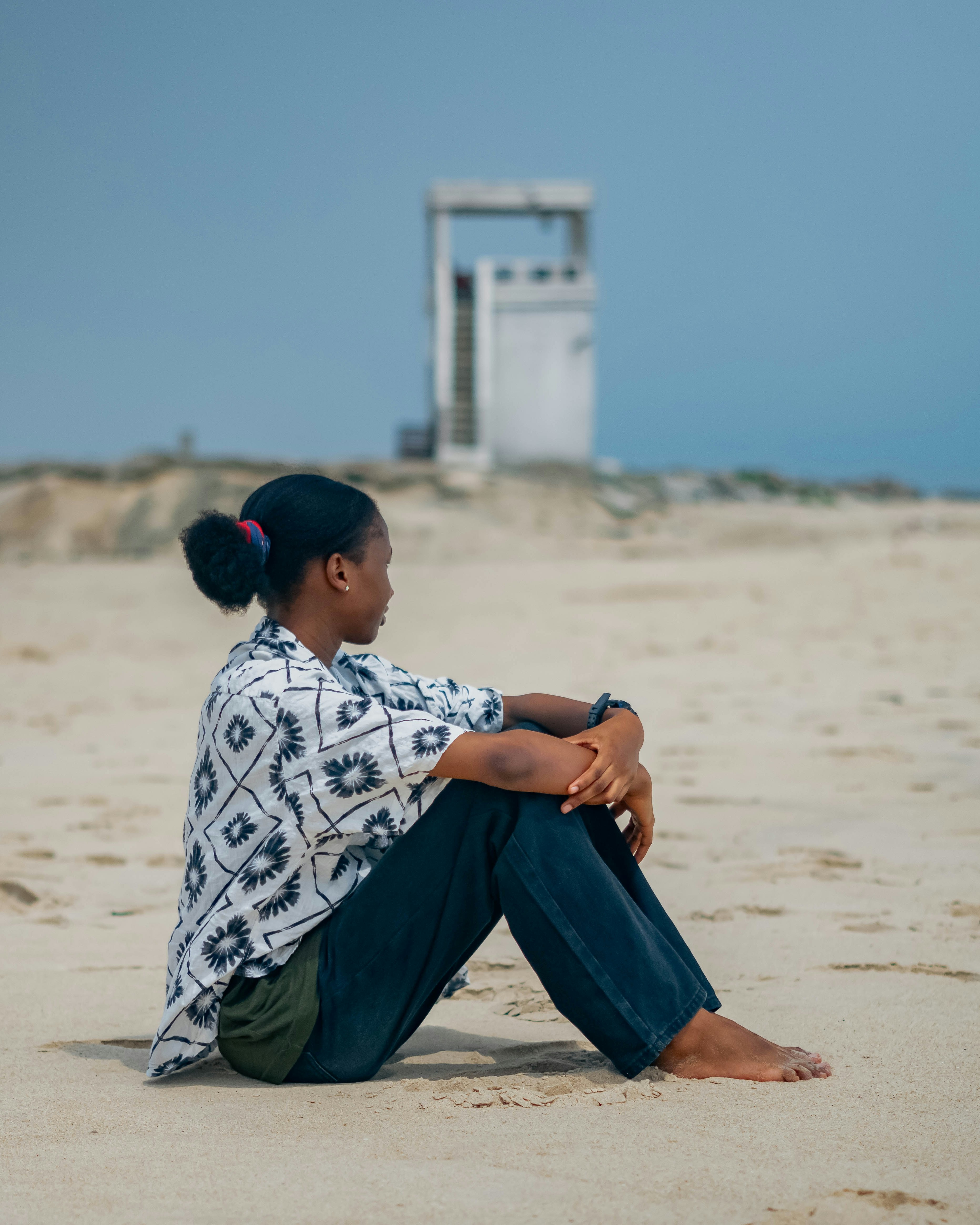Woman sits peacefully on a sandy beach.
