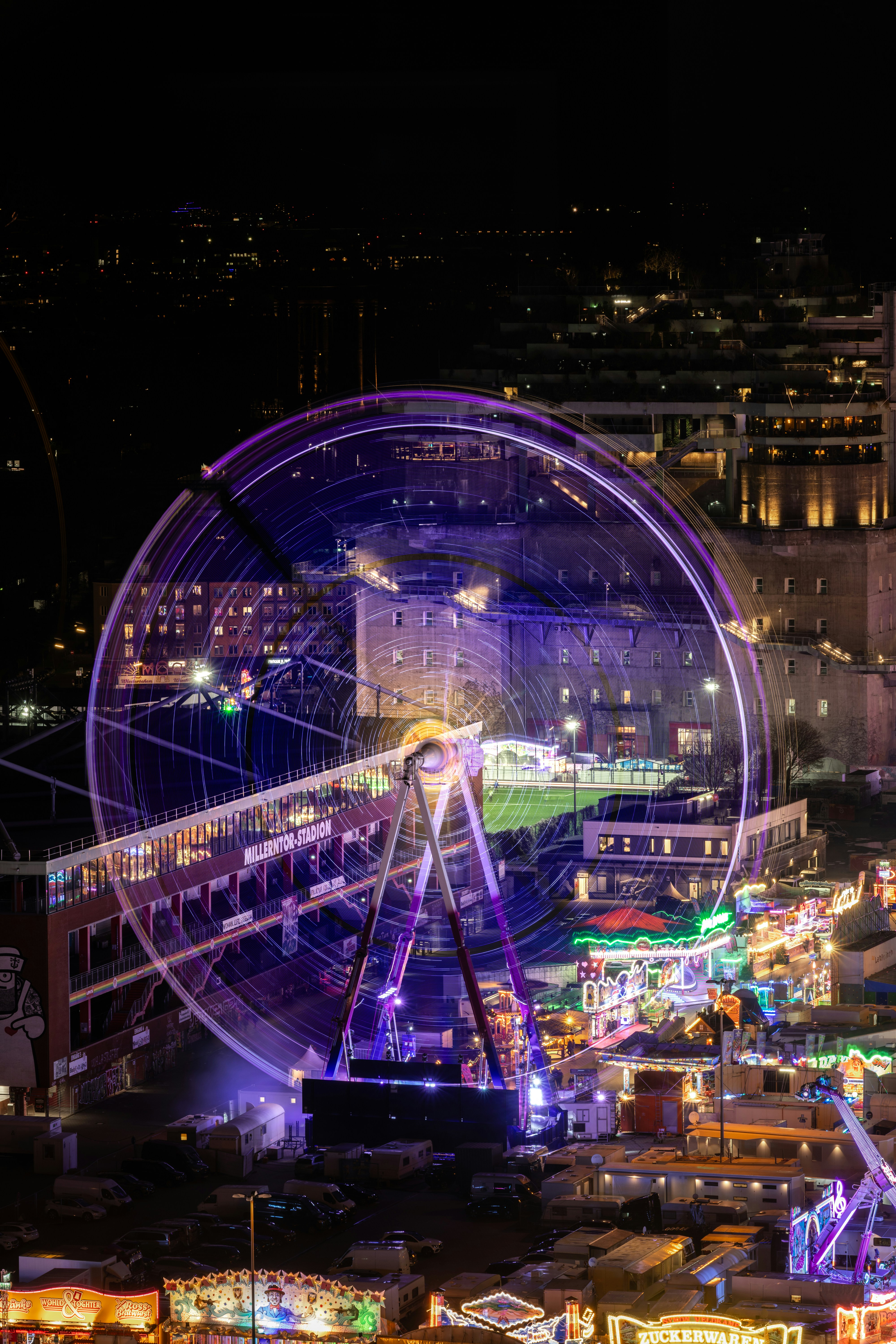 A ferris wheel spins with colorful lights at night.