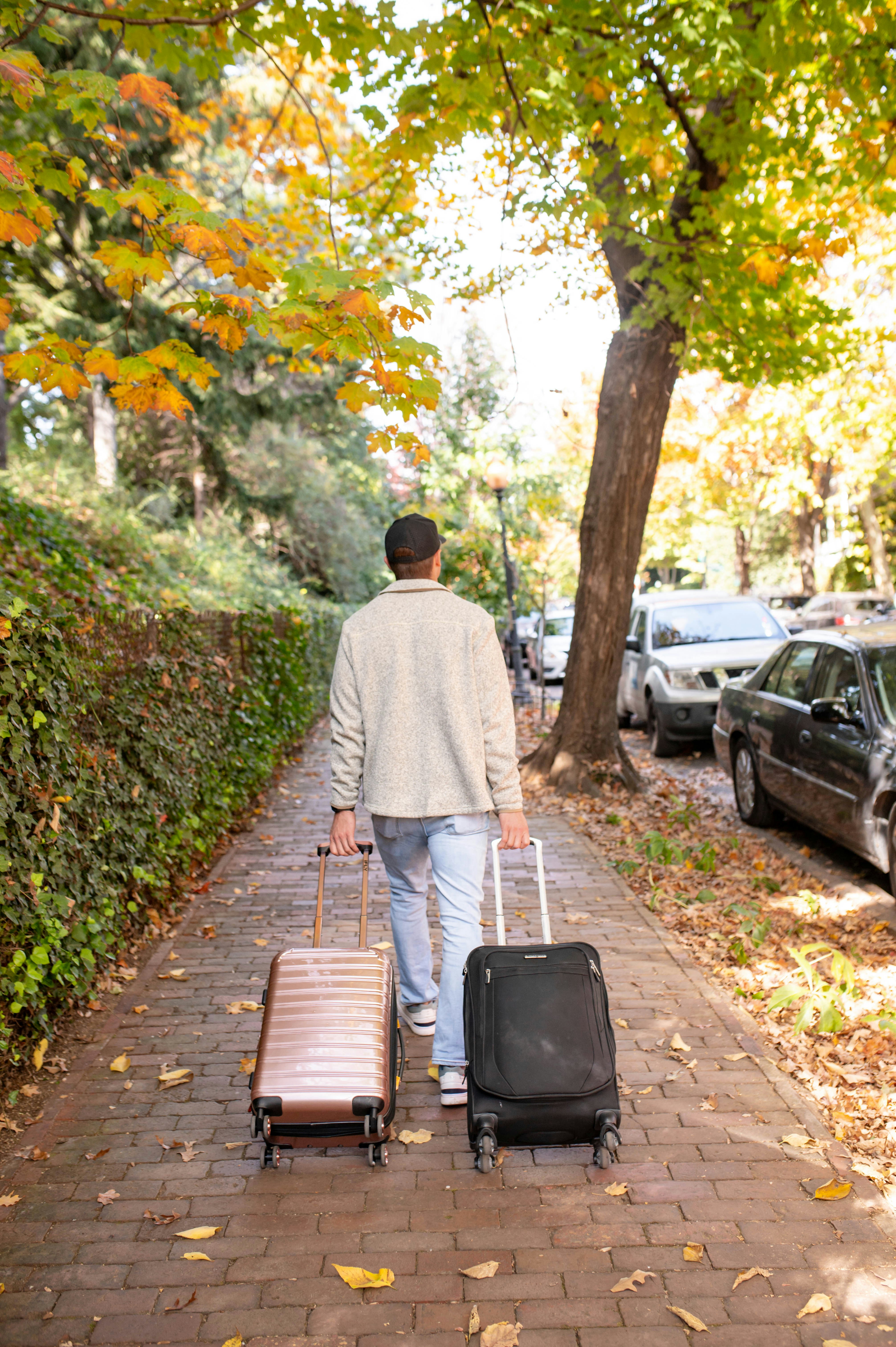 Man walks down a sidewalk with luggage.