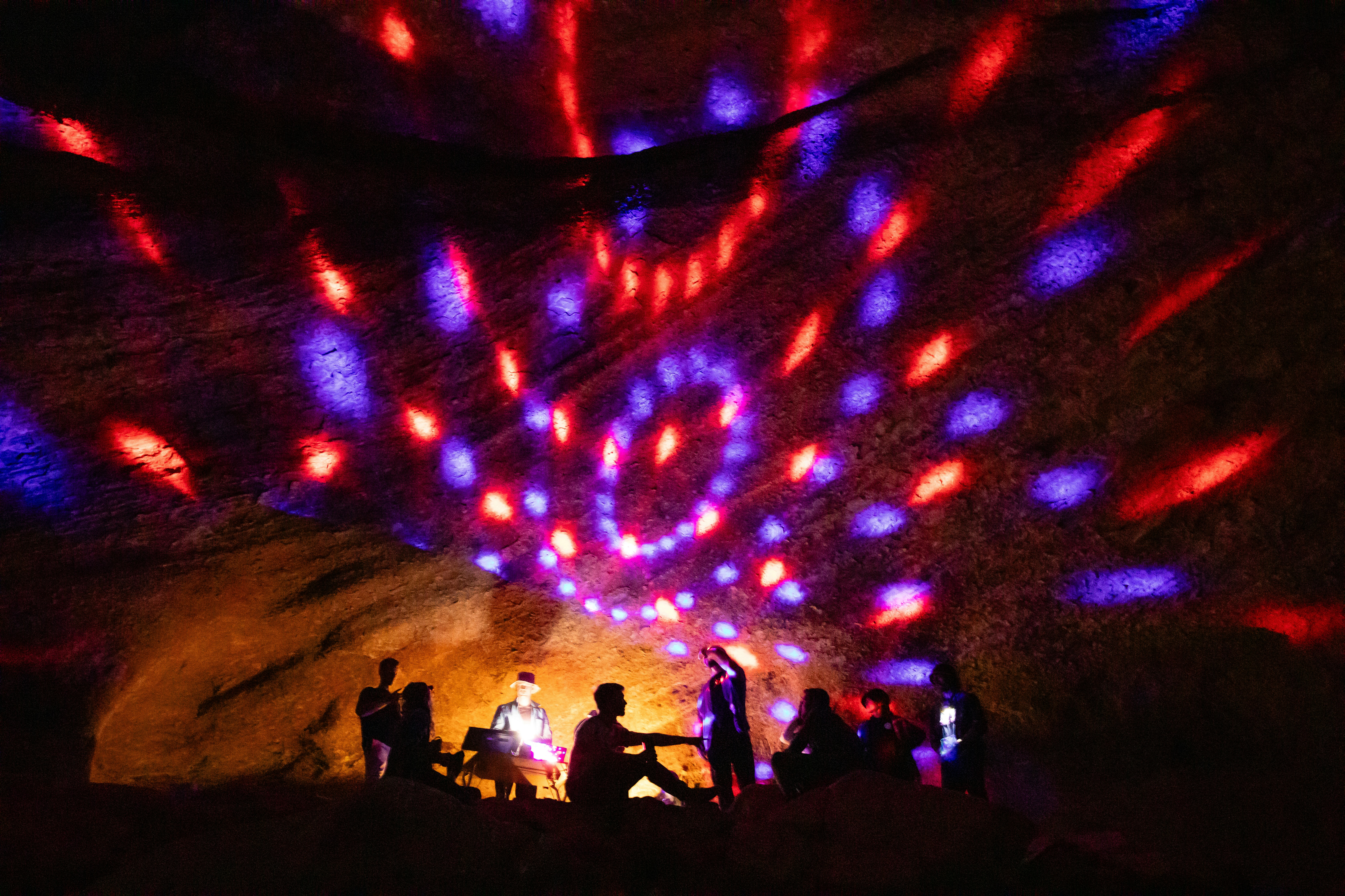 People are camping in a cave with colored lights.