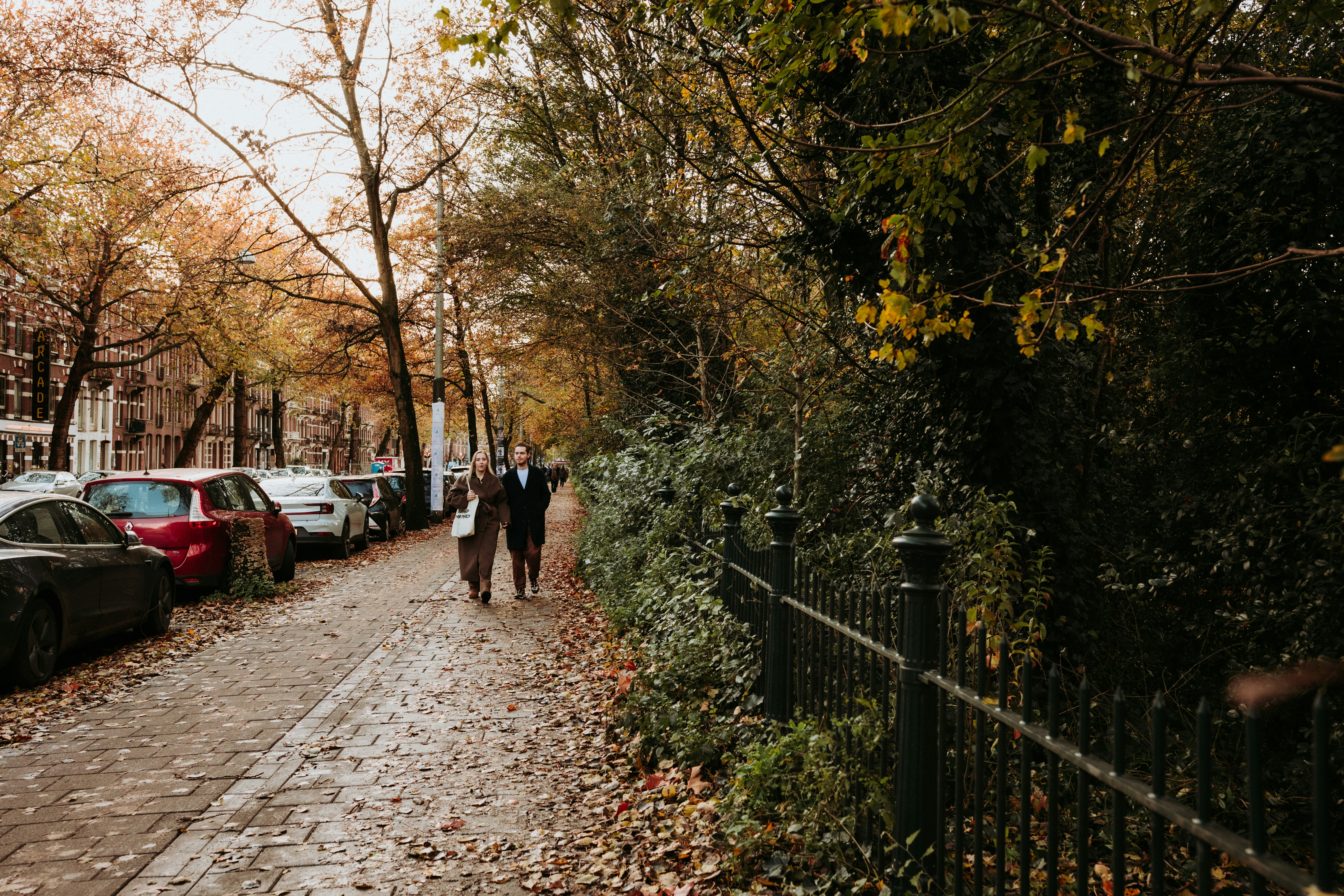 People stroll down a sidewalk lined with trees.