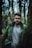 Man in green jacket poses in a forest.