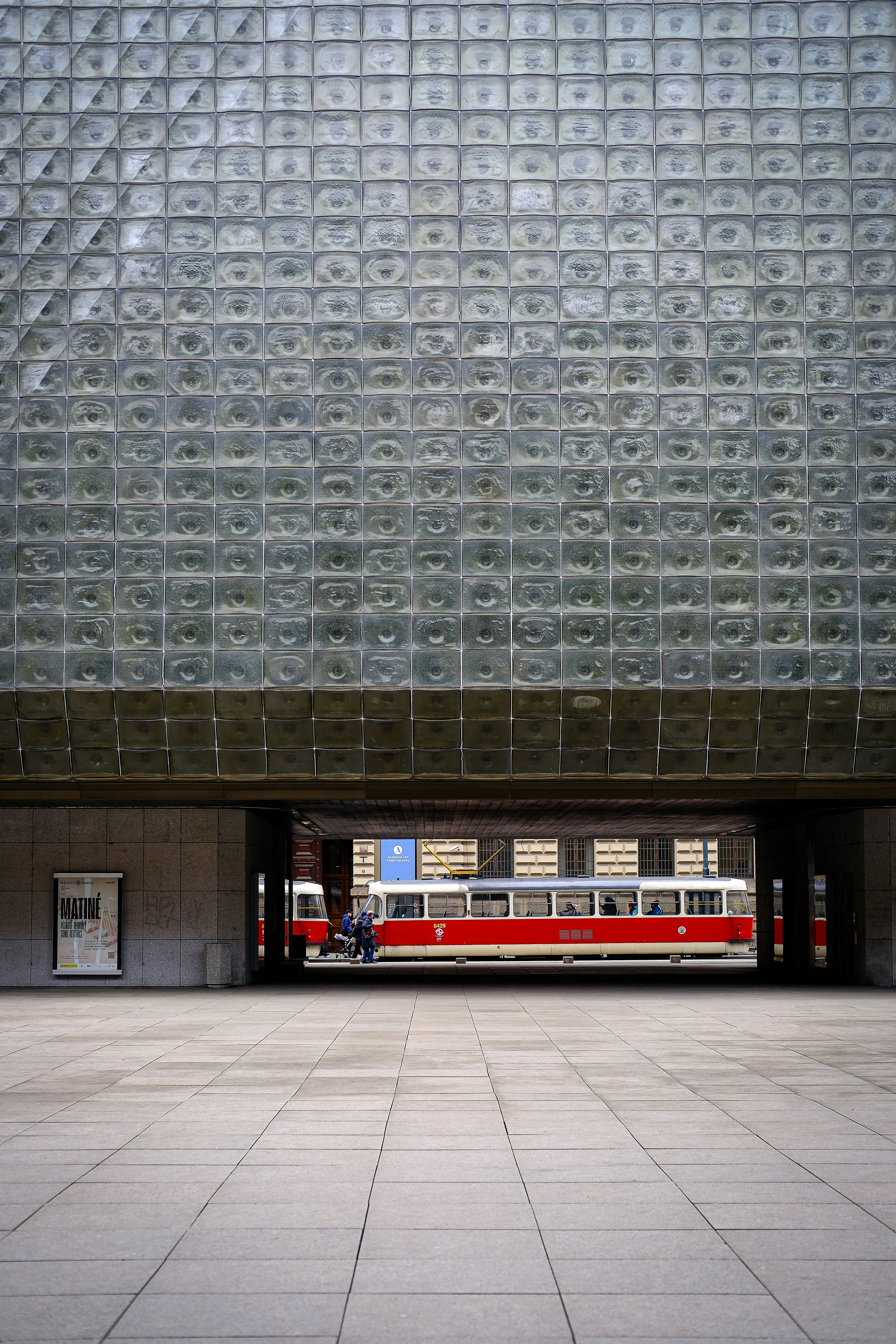 A red tram travels under a unique building.