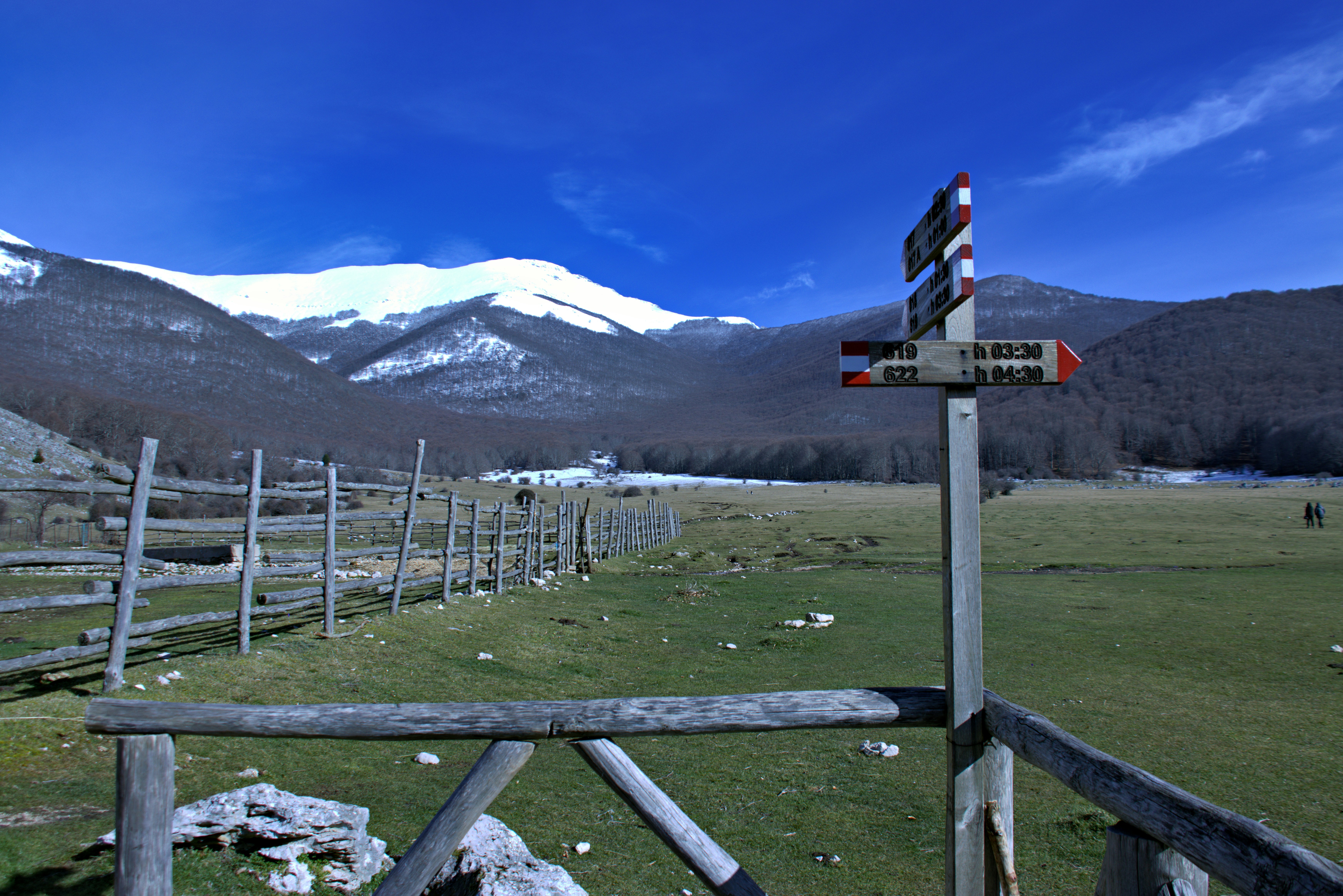 A sign directs hikers near a snow-capped mountain.
