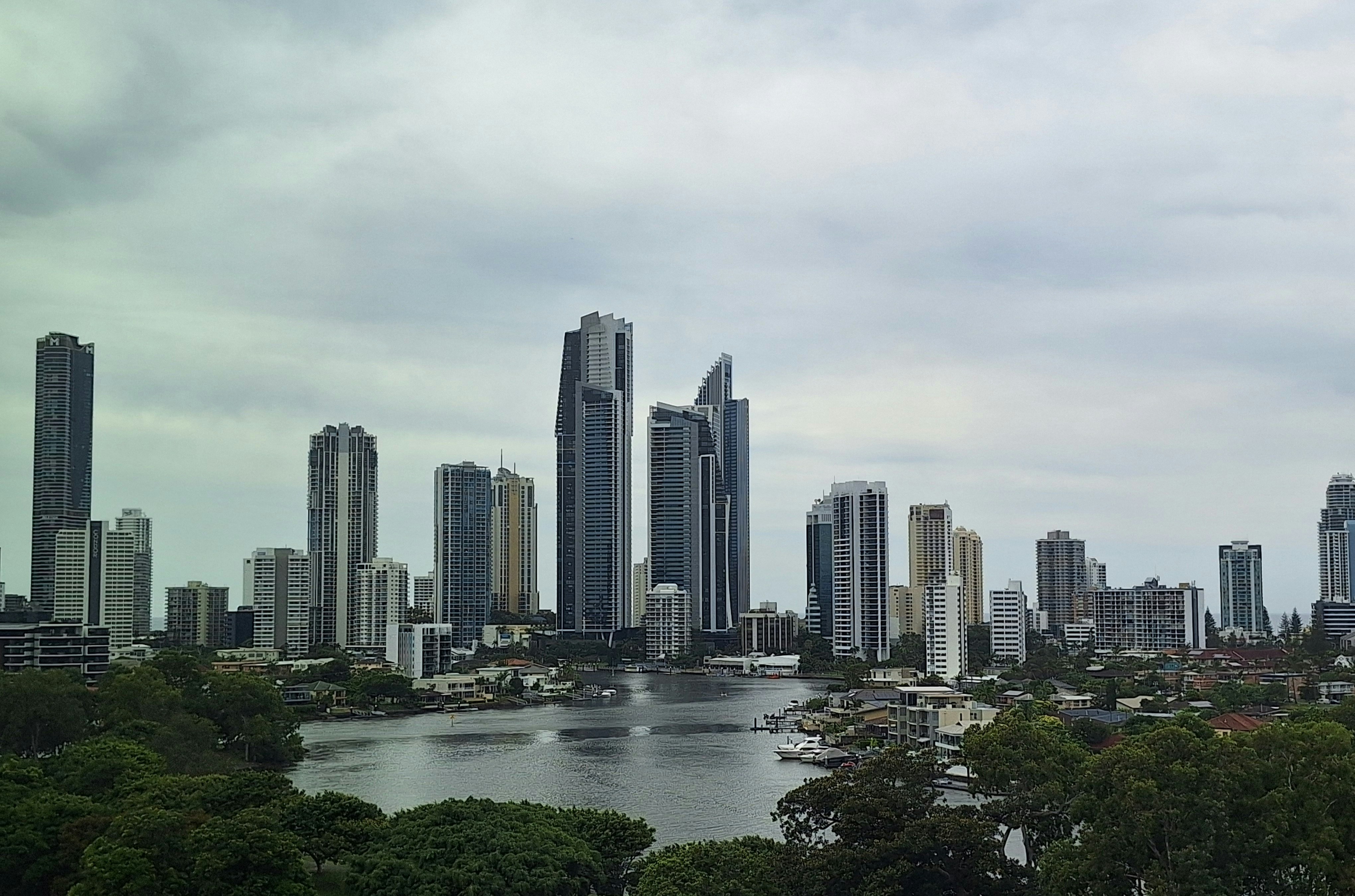 Skyscrapers stand along a river with a cloudy sky.