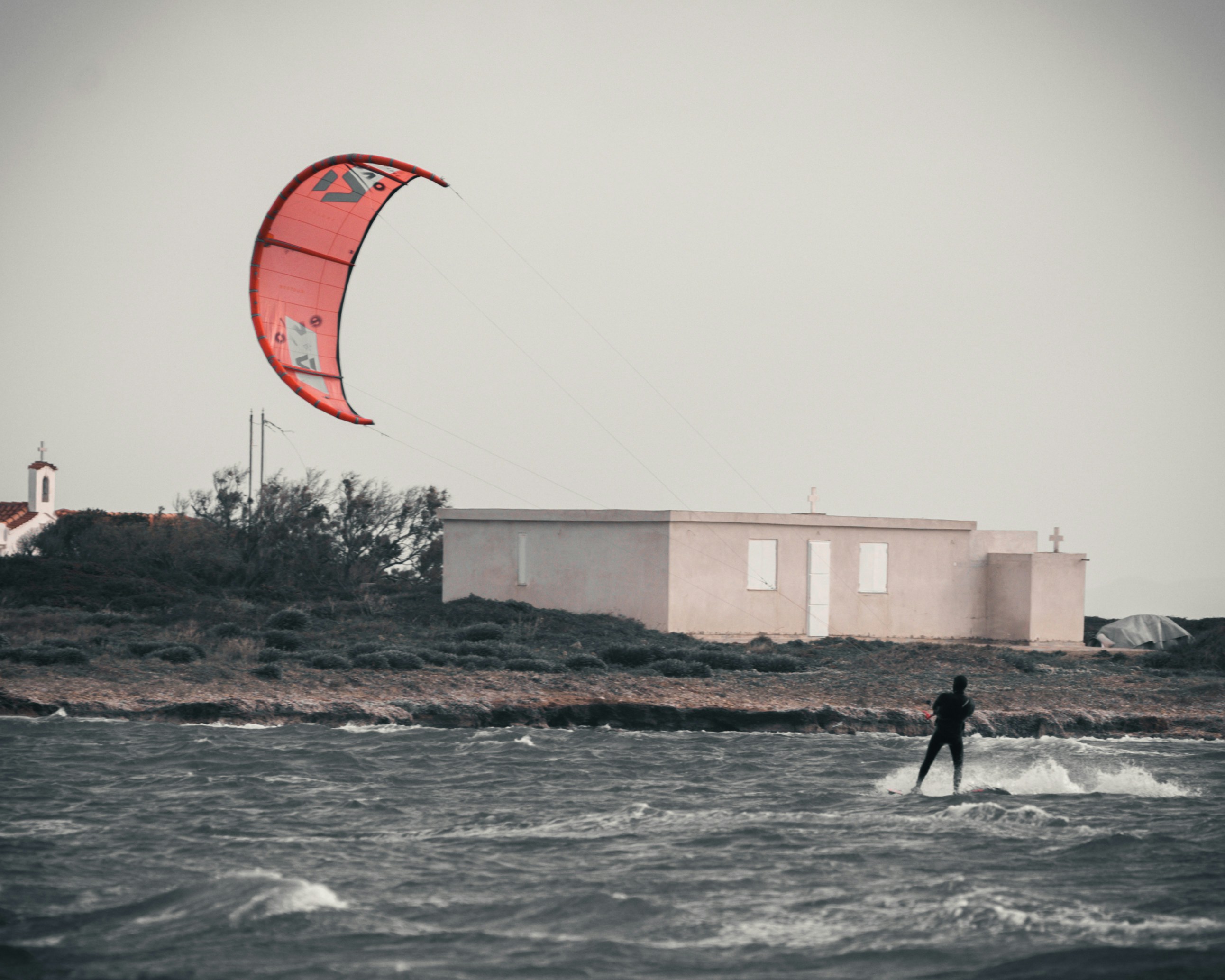 El kitesurfista disfruta de un día ventoso cerca de un edificio costero.
