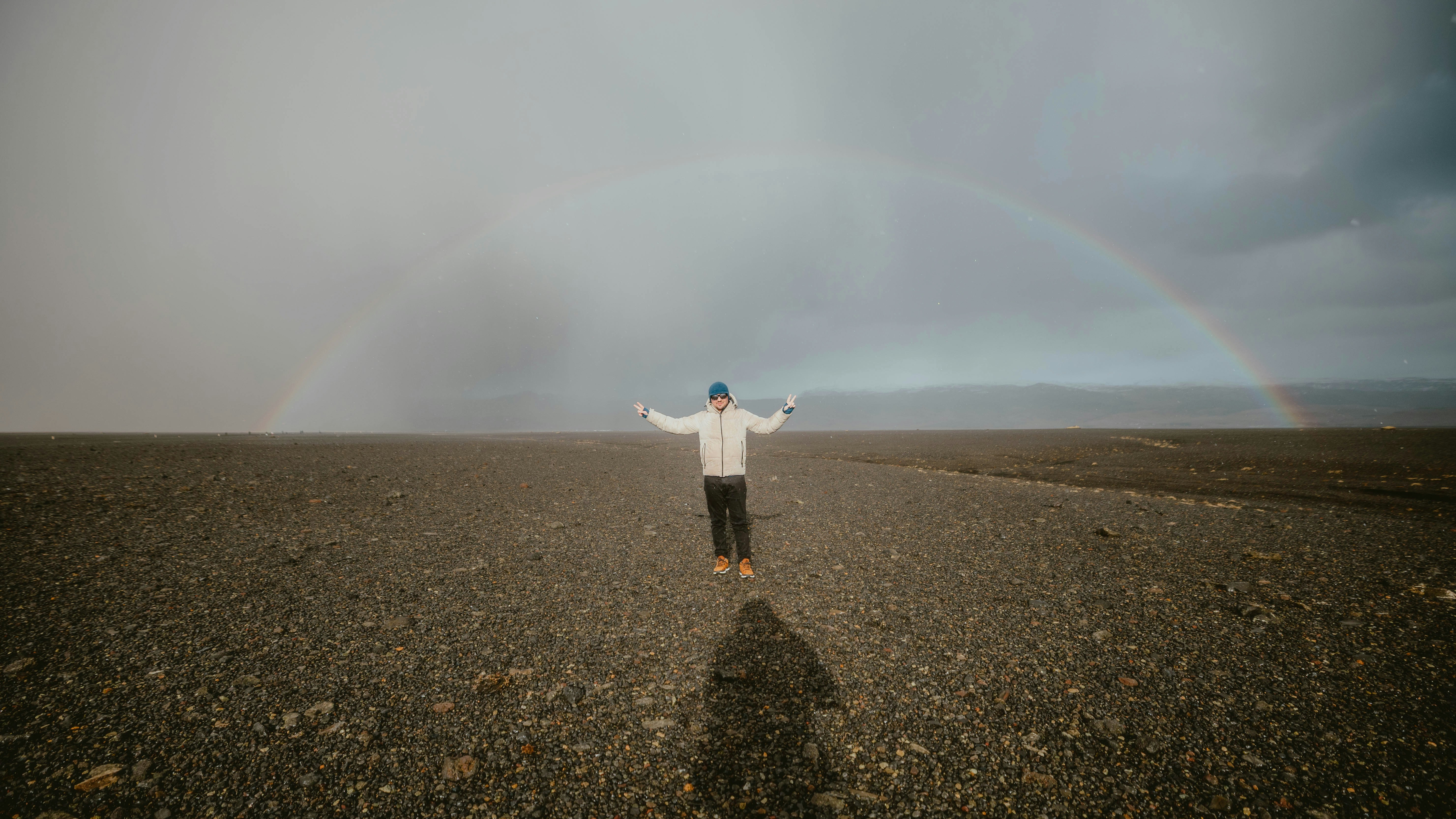Man stands under a double rainbow with open arms.