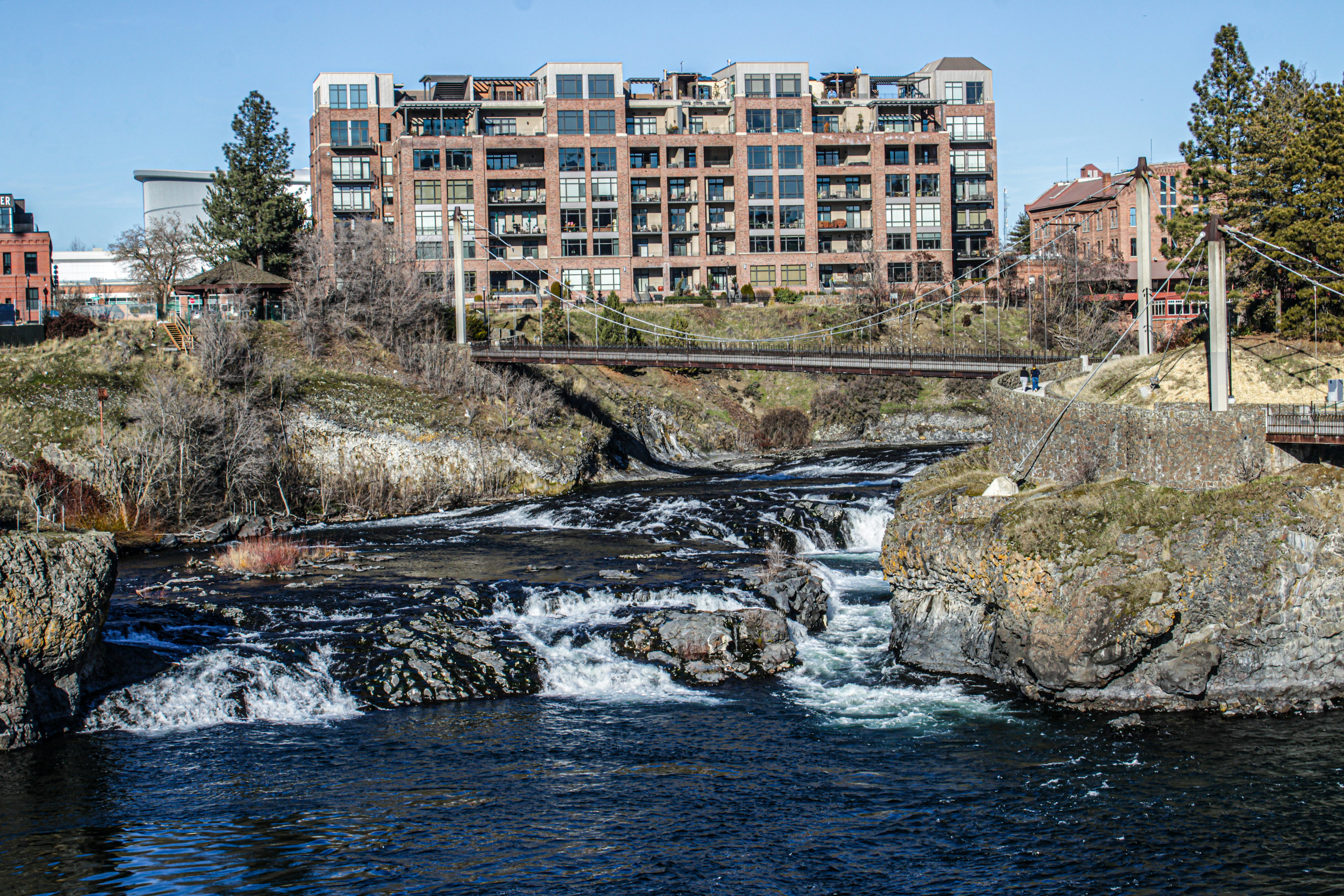 Waterfall flows under a bridge with building in background.