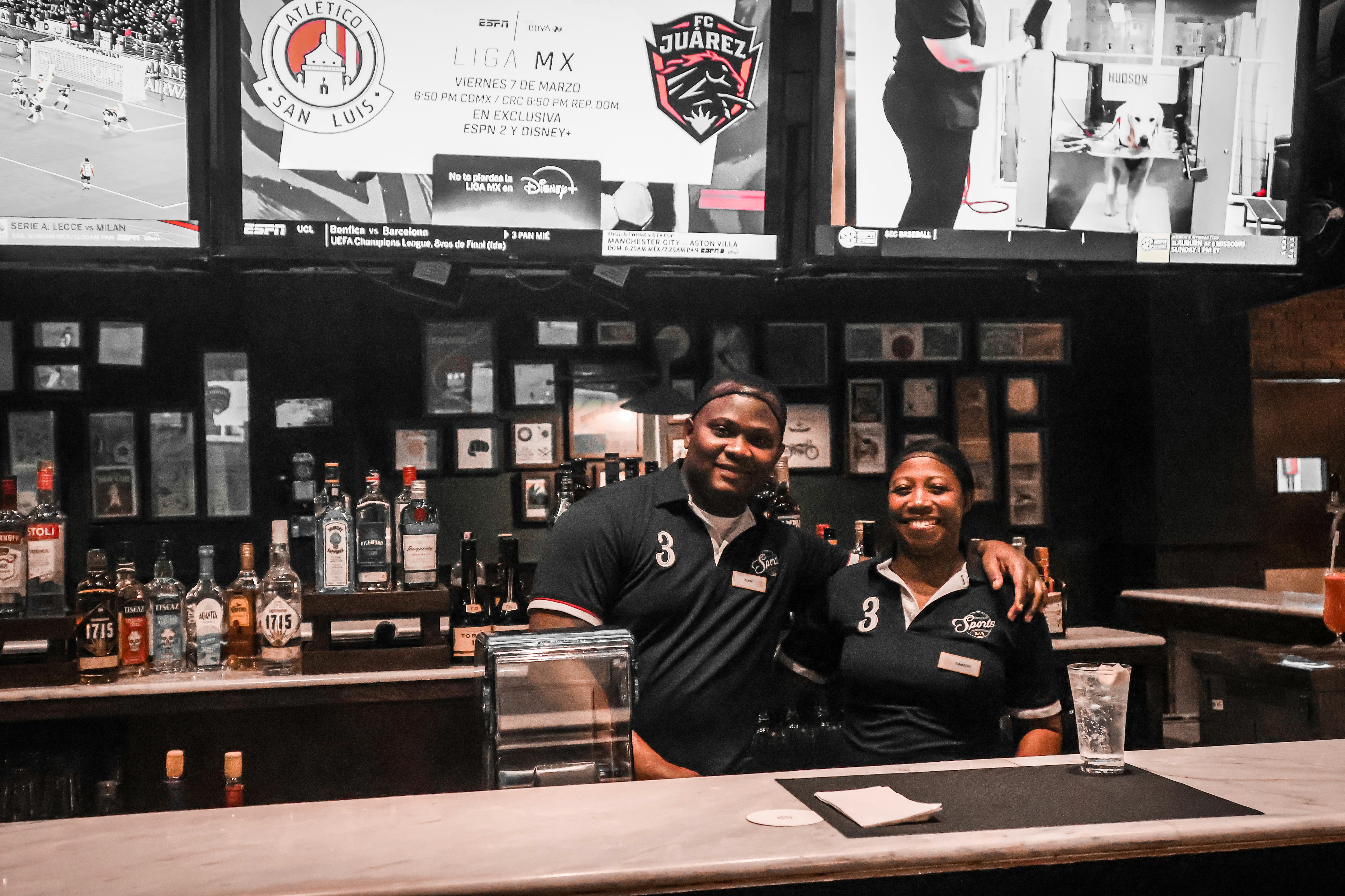 Personas viendo un partido en pantallas grandes y revisando cuotas