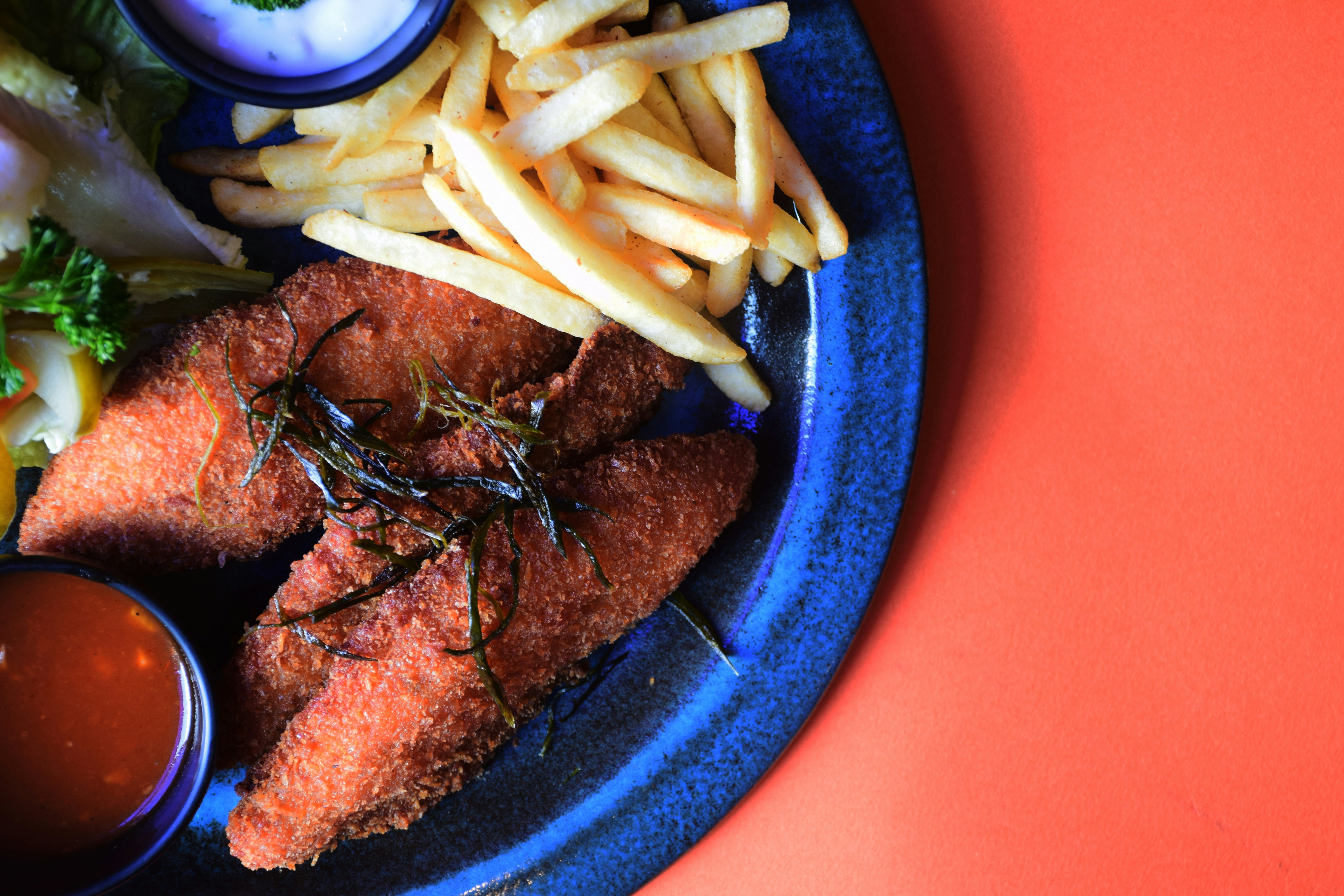 Fried fish, fries, and sauces on a plate.