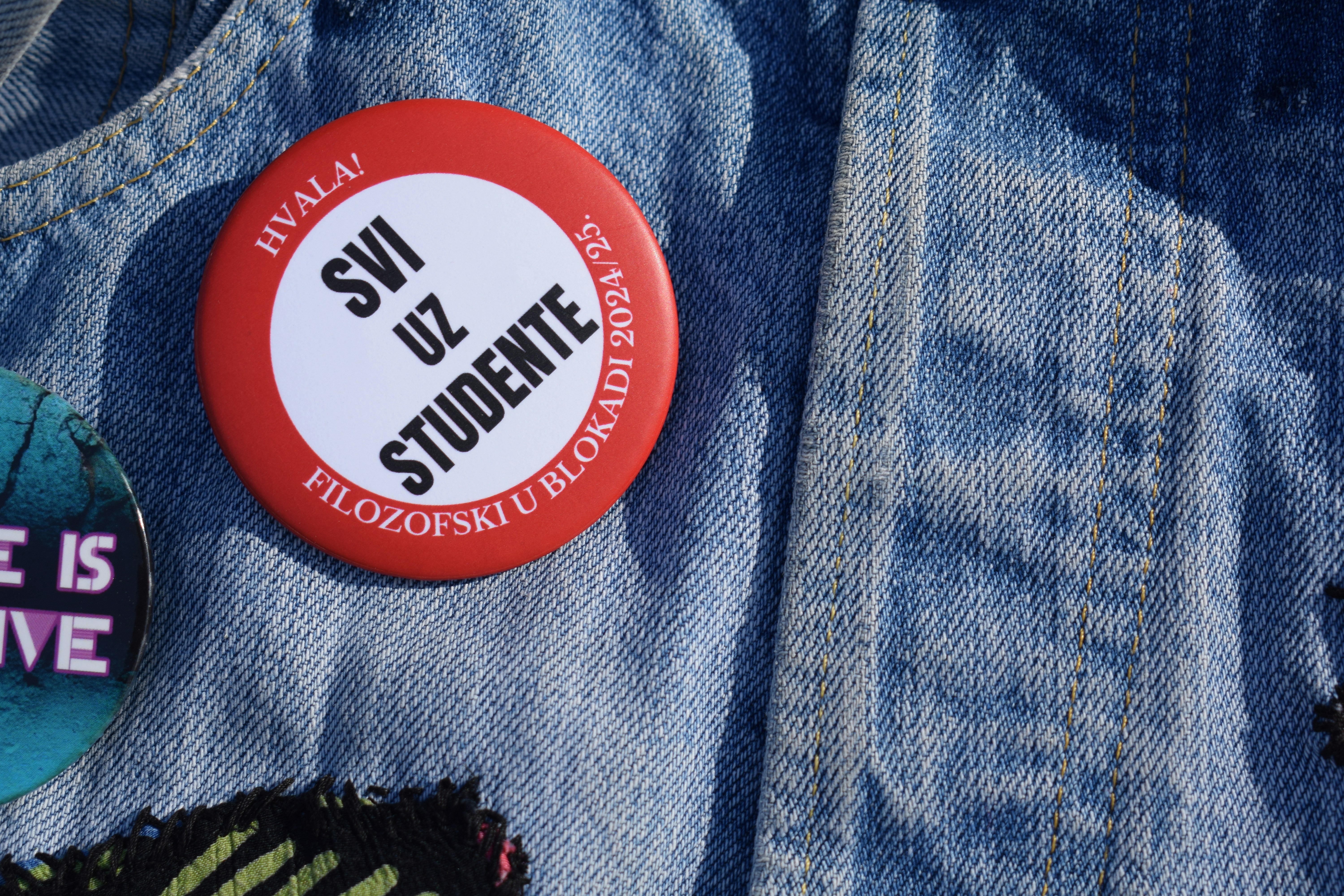 Button on denim says, "support students."