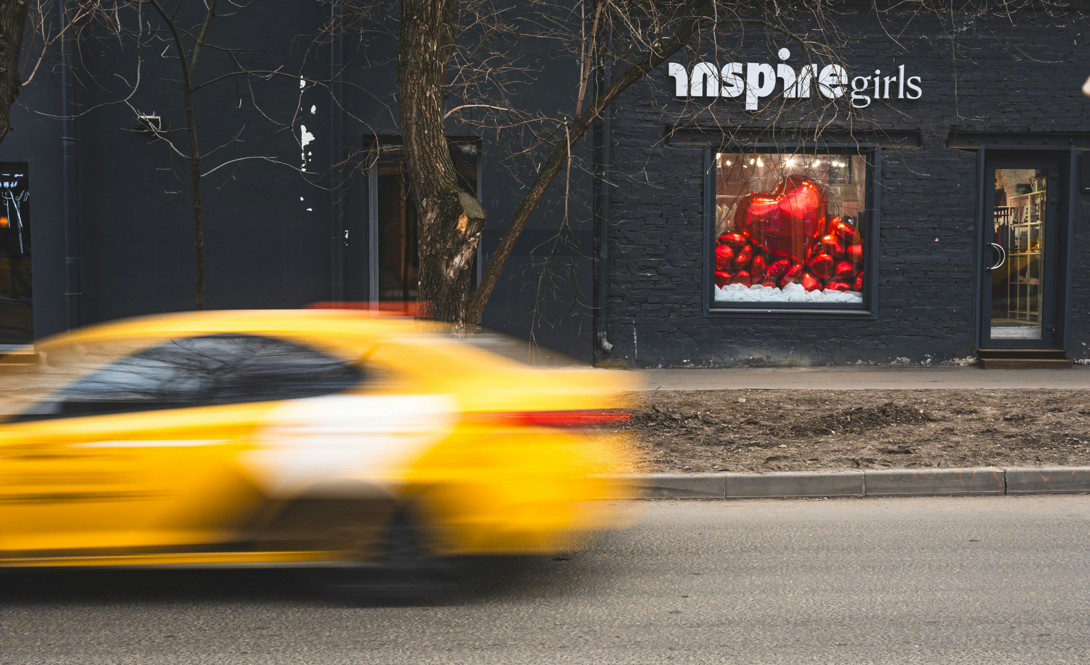 A yellow car drives past a storefront.