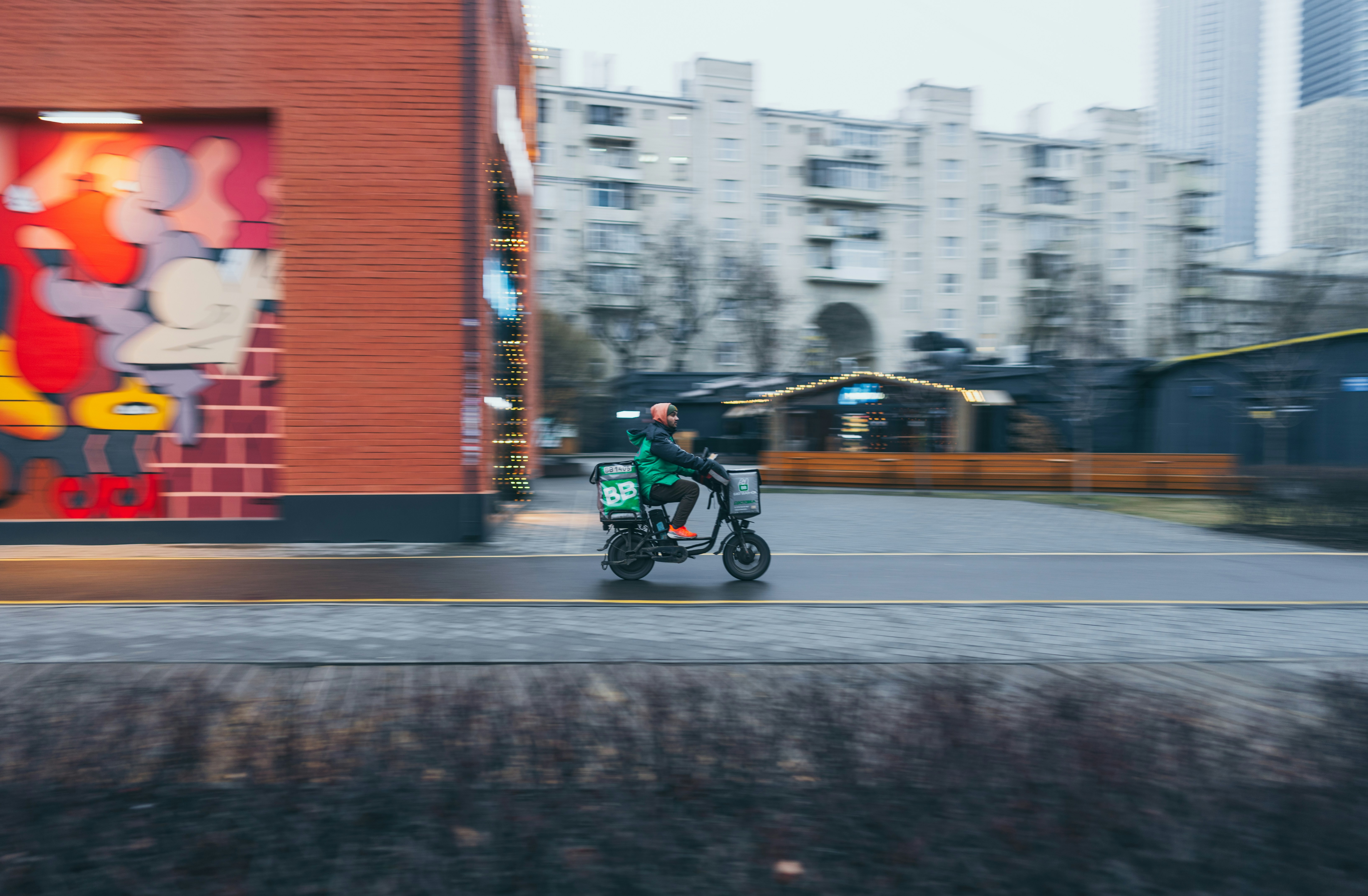 Delivery driver rides a scooter through the city street.