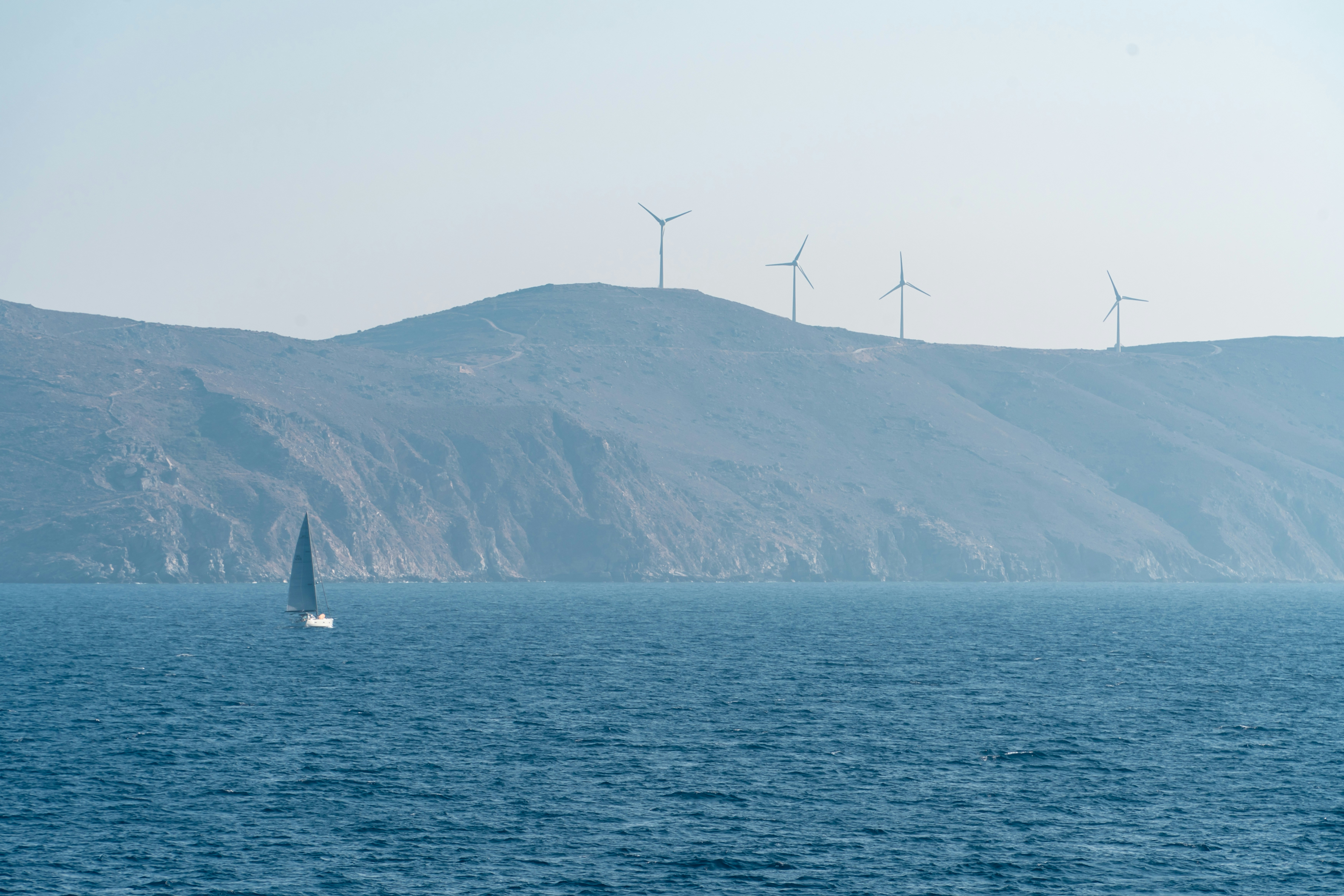 A sailboat glides past wind turbines on a hill.