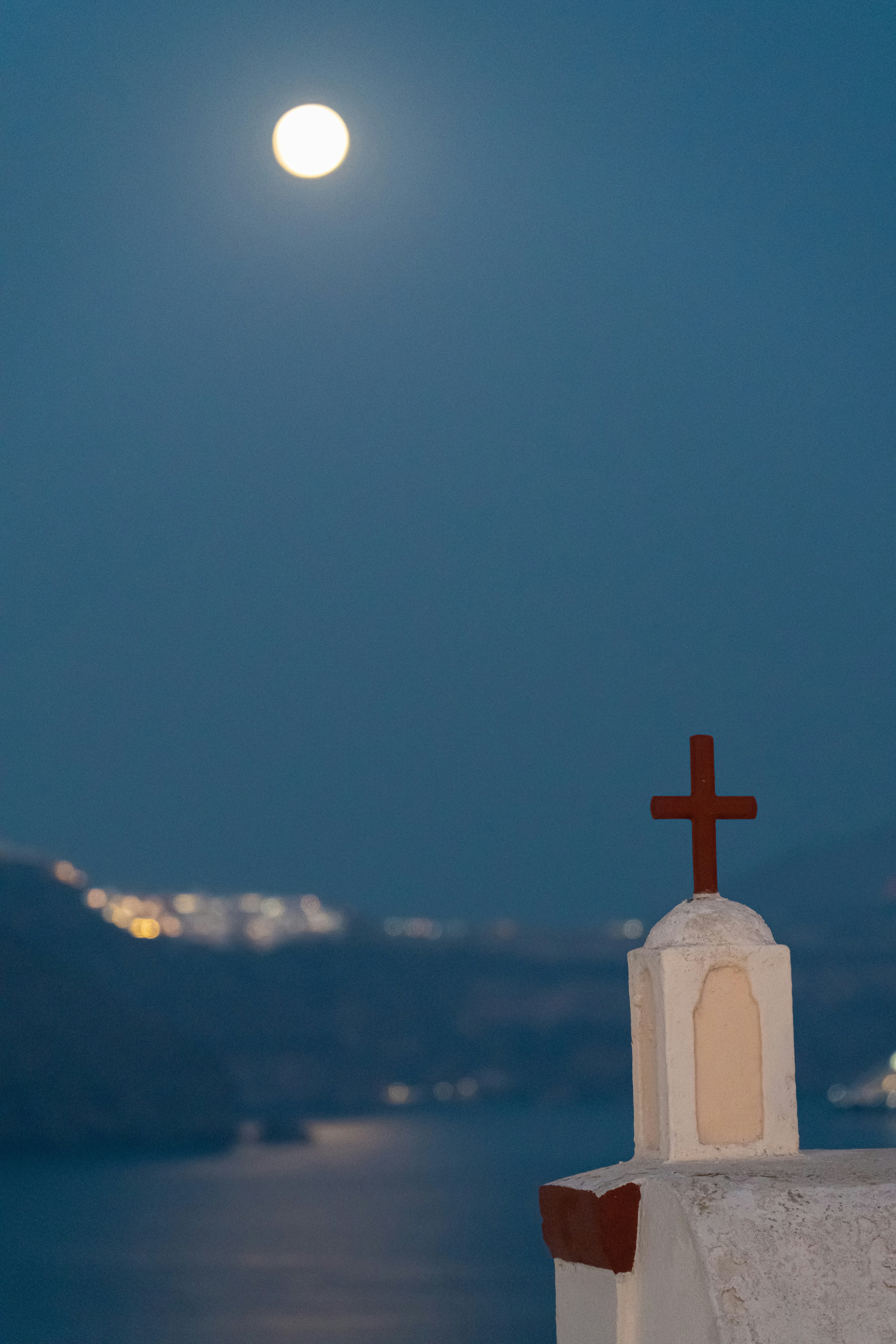 Moon shines above a church cross at night.