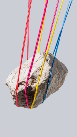 A rock is suspended by colorful strings.